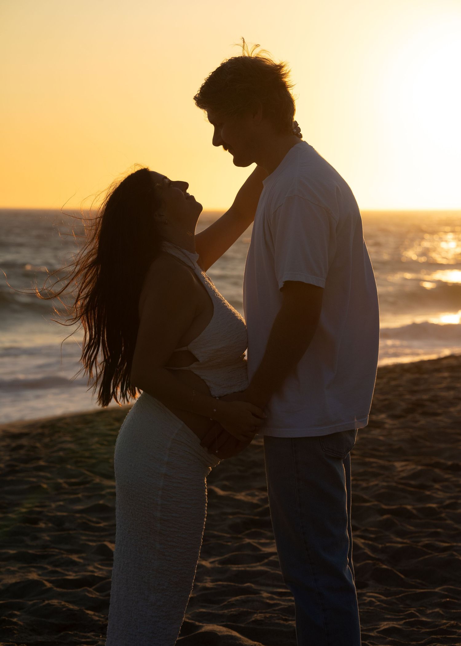 Silhouetted figures share tender moments against dramatic beach sunset.