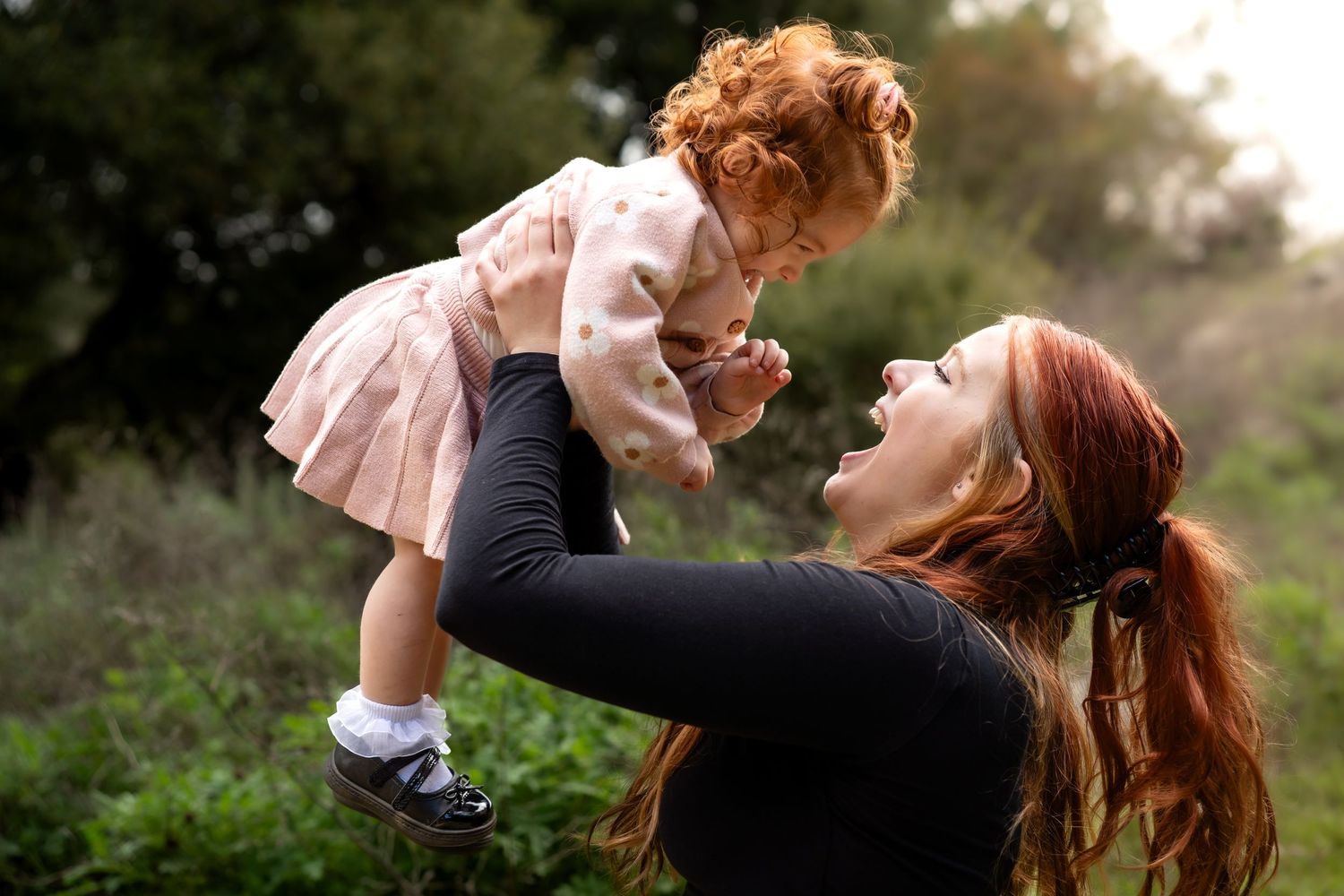 A joyful moment captured as a parent lifts a small child wearing a pink dress outdoors.