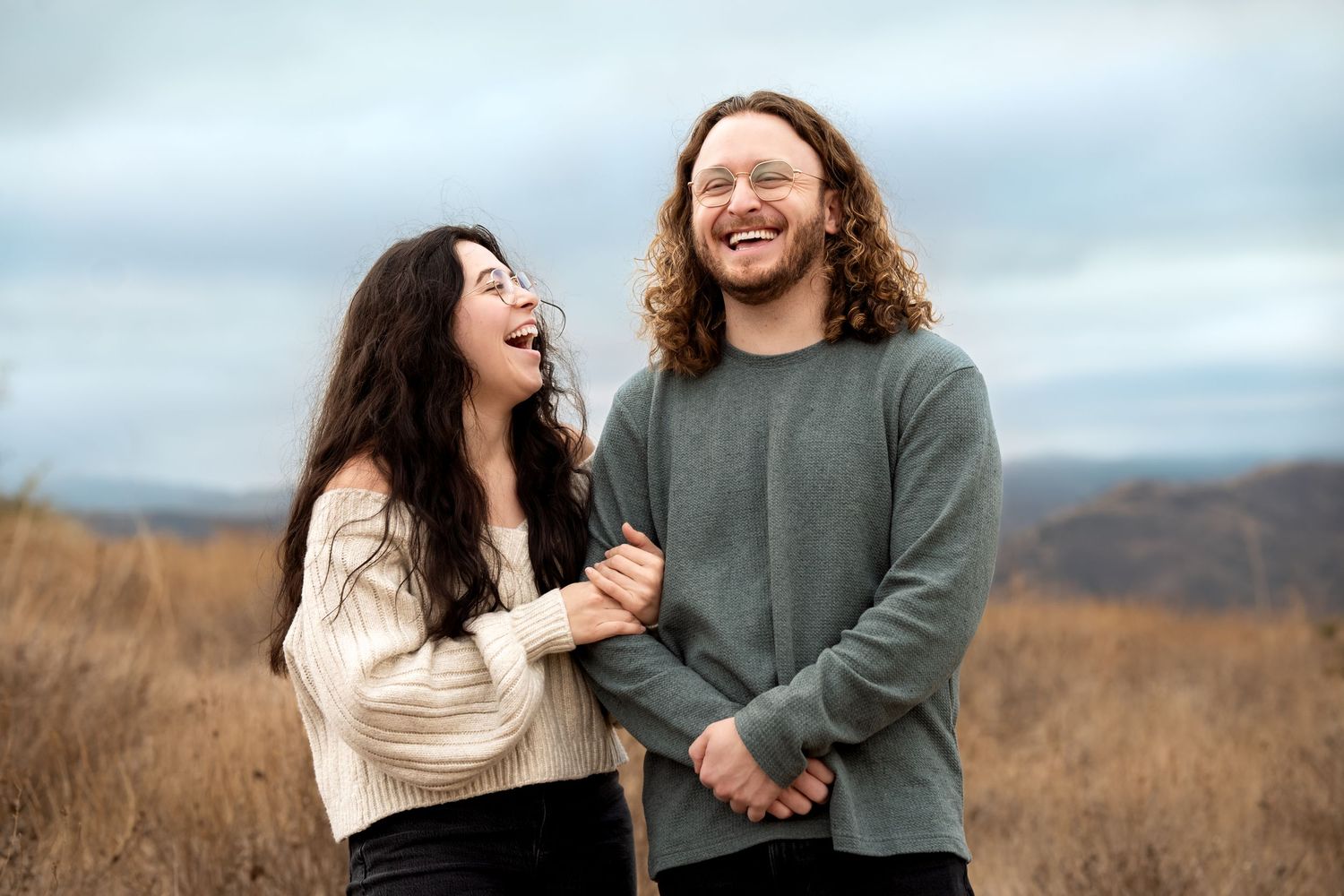 Joyful couple laughing together in open field wearing casual sweaters.