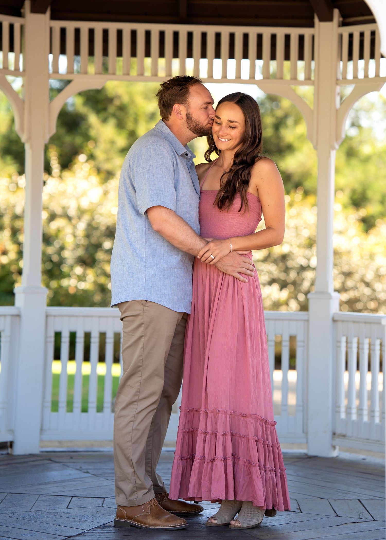 Romantic couple embracing under white gazebo in afternoon sunlight.
