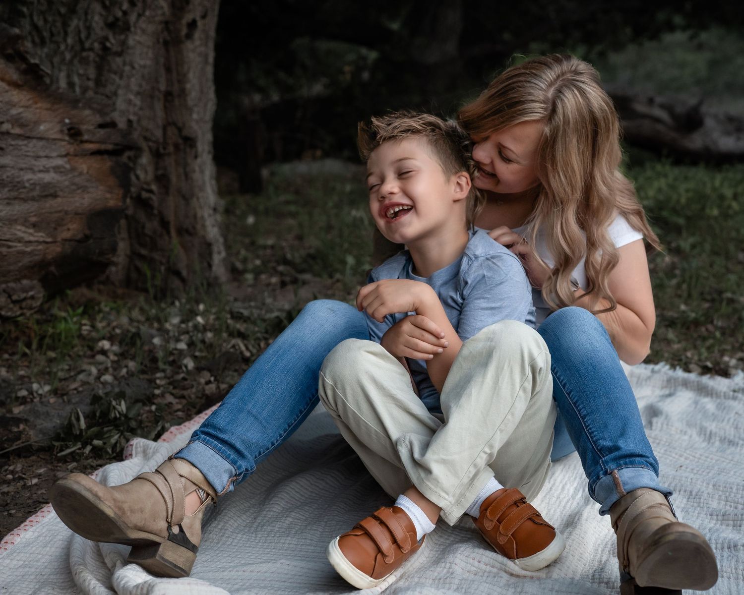 A candid moment of laughter and embrace while sitting on a blanket outdoors.