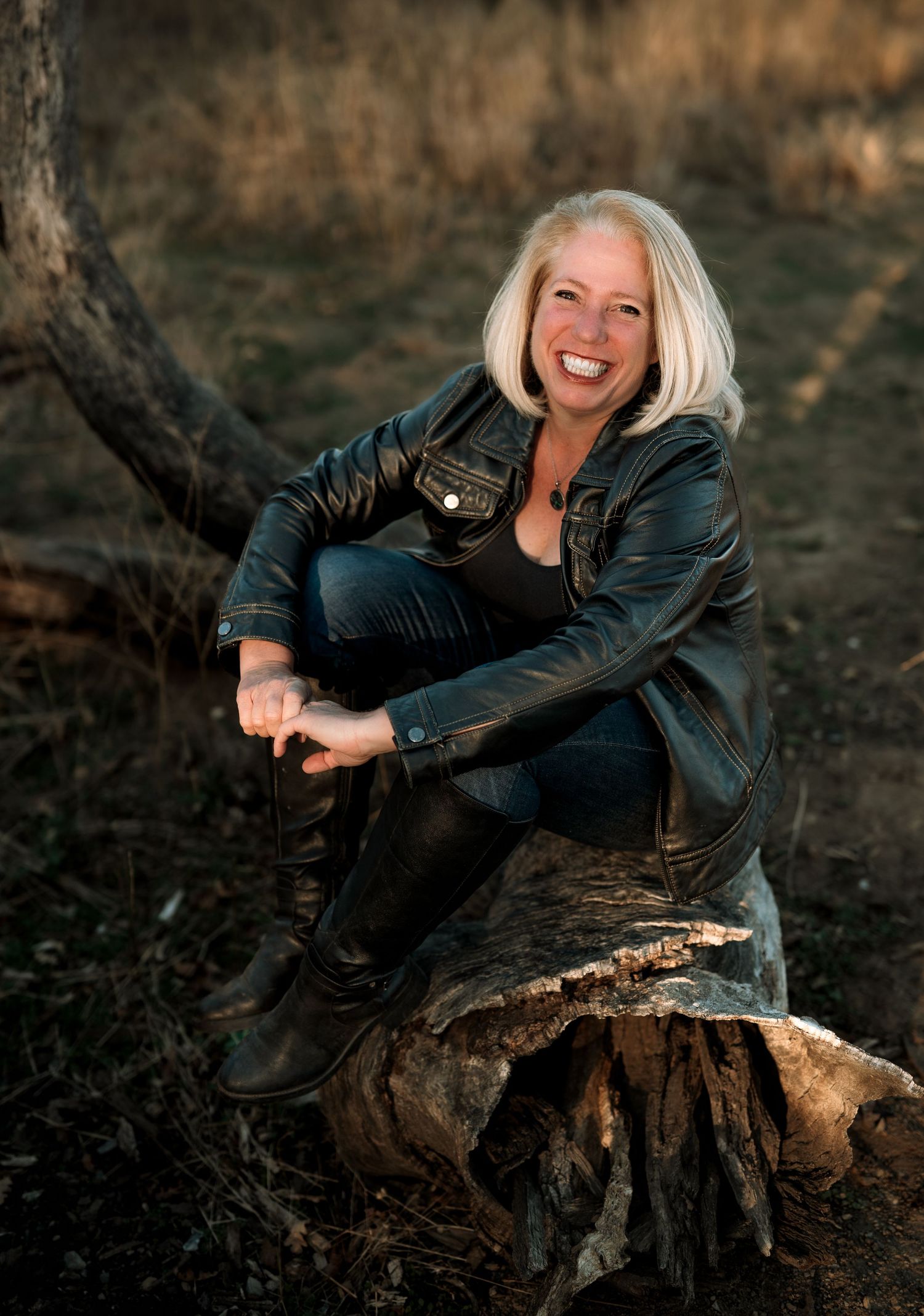 Casual portraits on a wooden log featuring a black leather jacket at sunset.