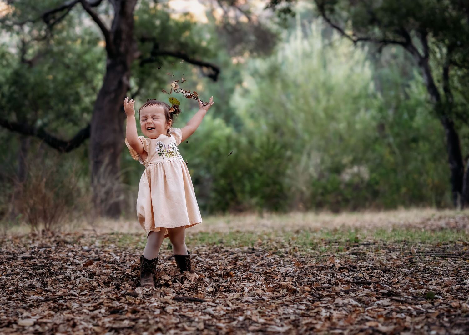 Small child walking through fallen autumn leaves in a pink dress.