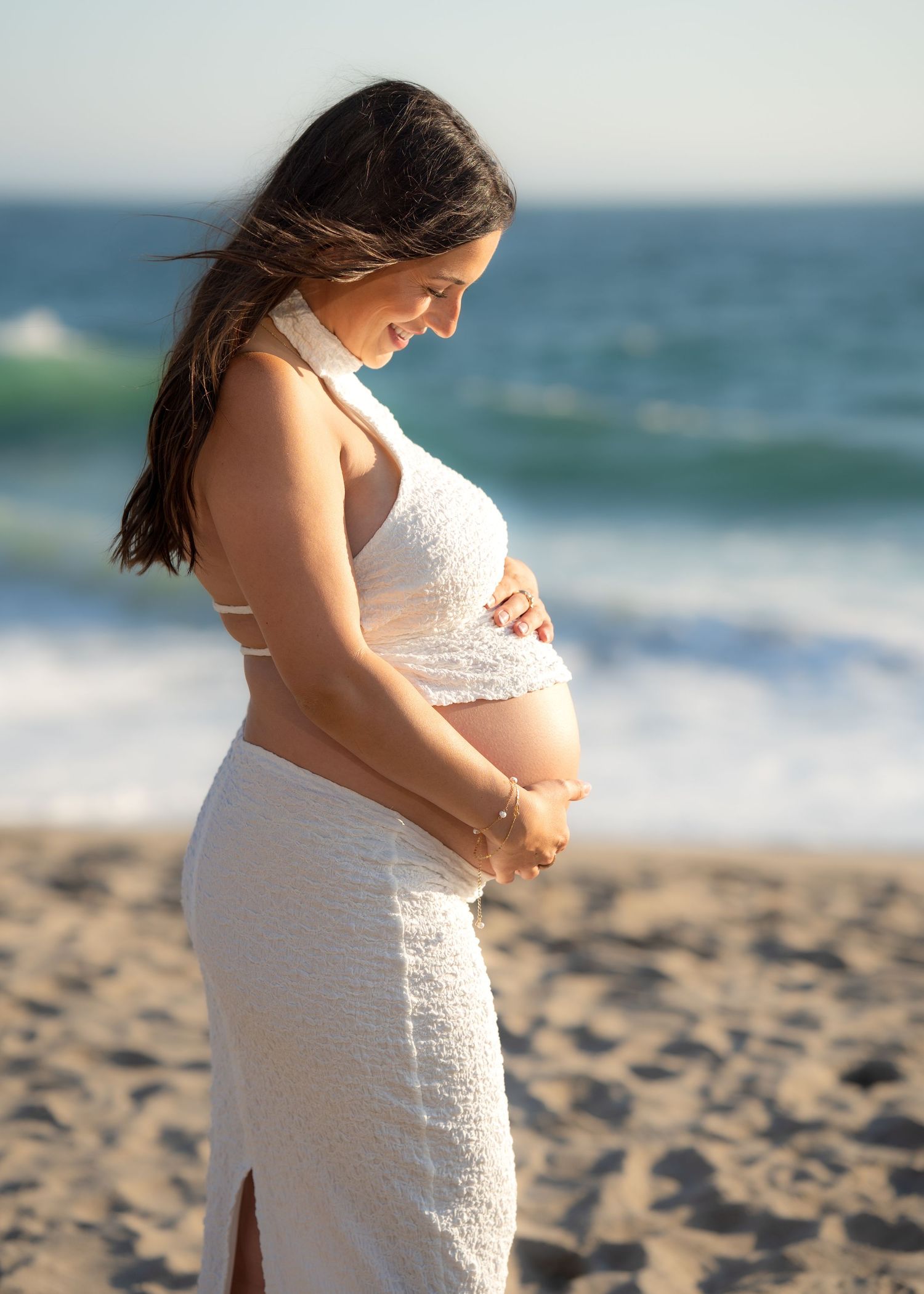 Peaceful maternity photos captured on sandy beach with ocean waves in background.