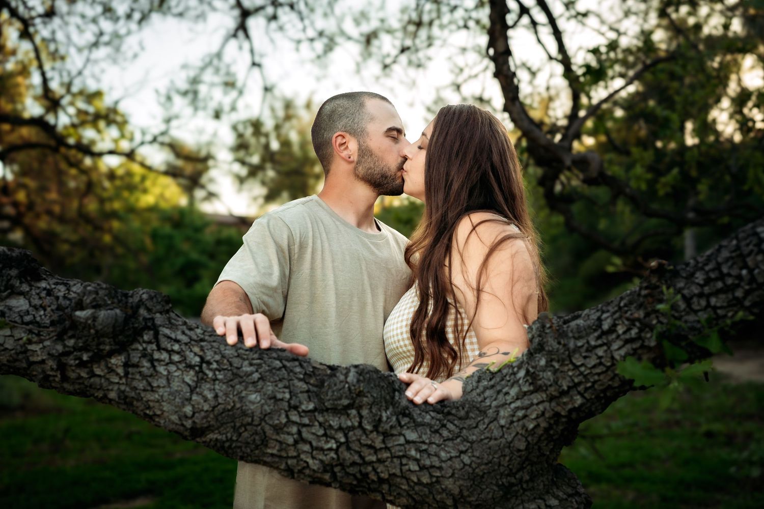 Couple sharing intimate moment under large tree branches.