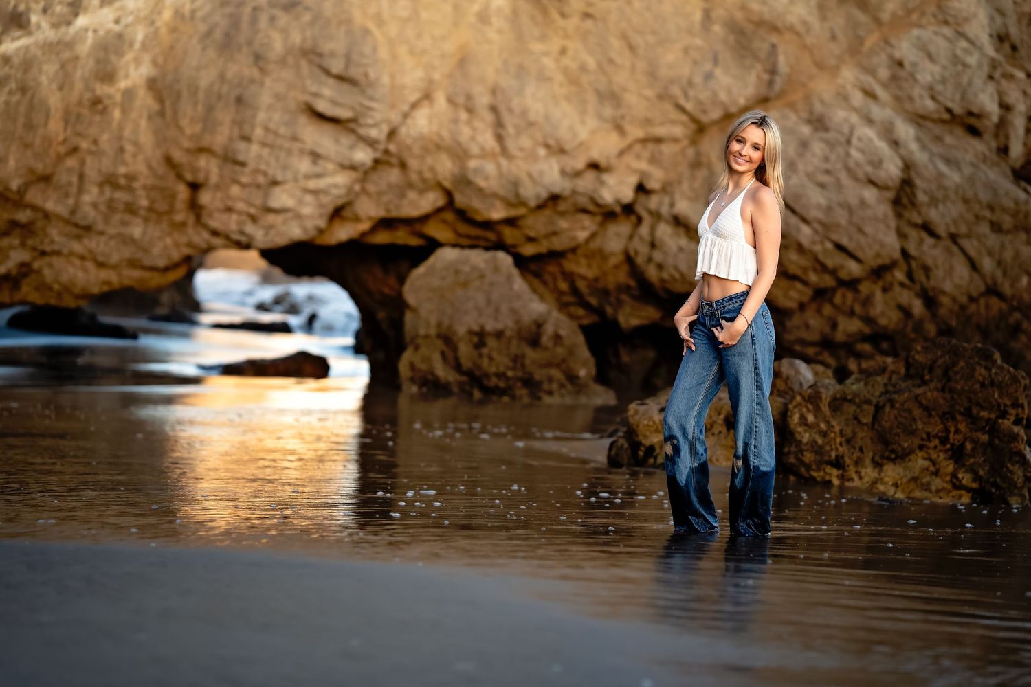 Couple poses near rocky cliffs at a beach during golden hour.
