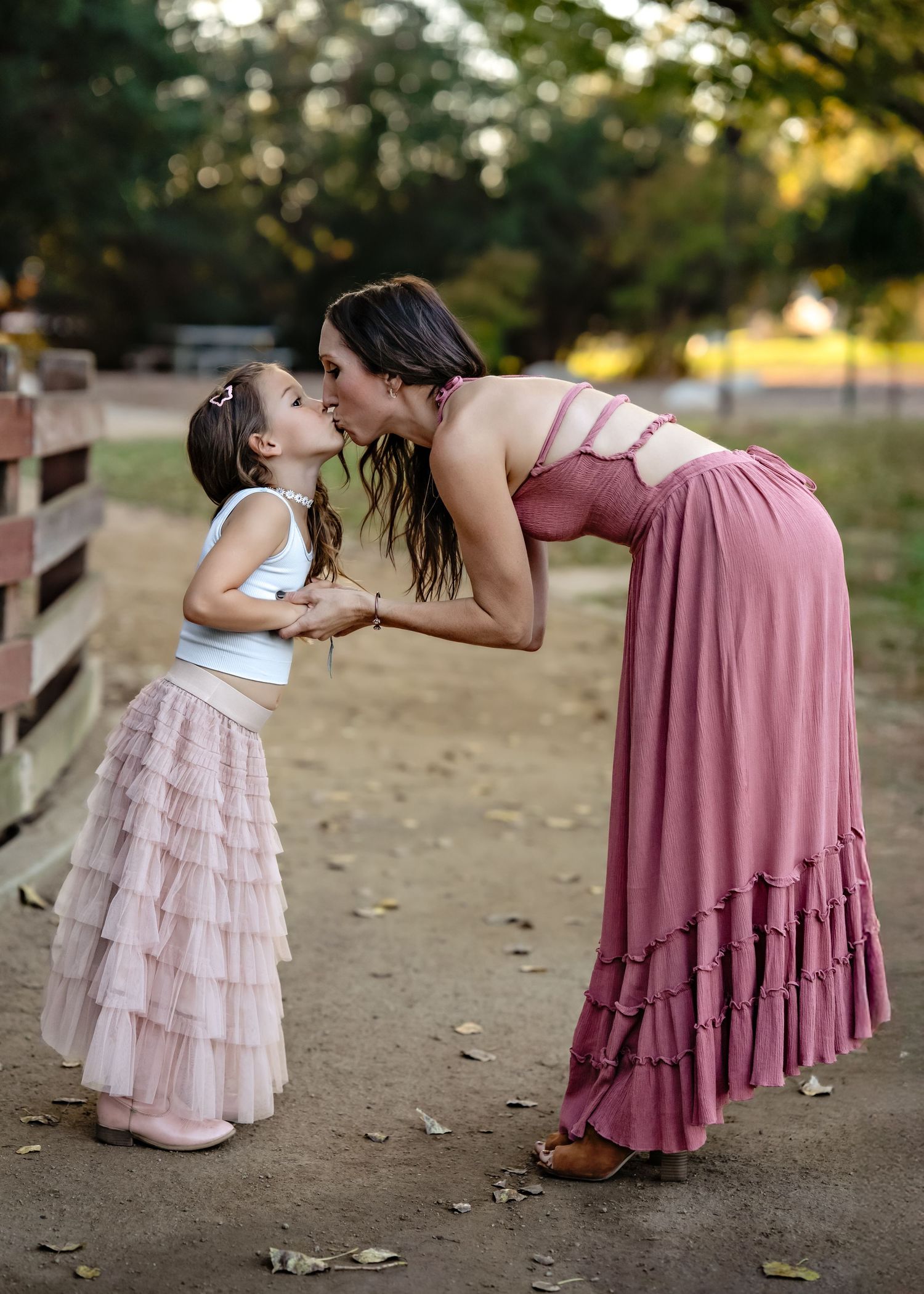 A parent and child in flowing dresses share a sweet moment together on a dirt path.