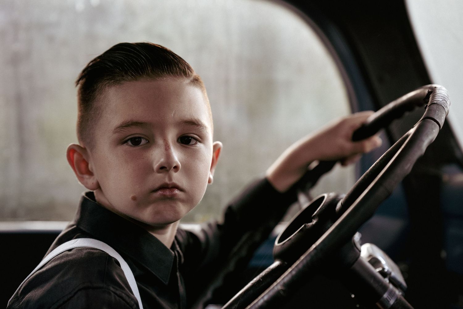 Young child sitting in car seat with serious expression in moody lighting.