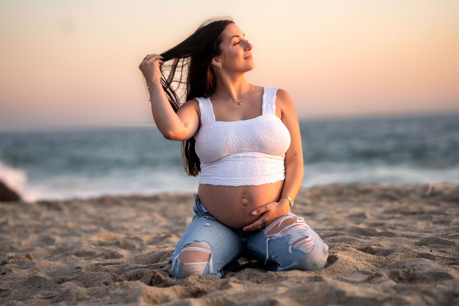 Intimate beachside photoshoot with couple sitting on sand during golden hour.