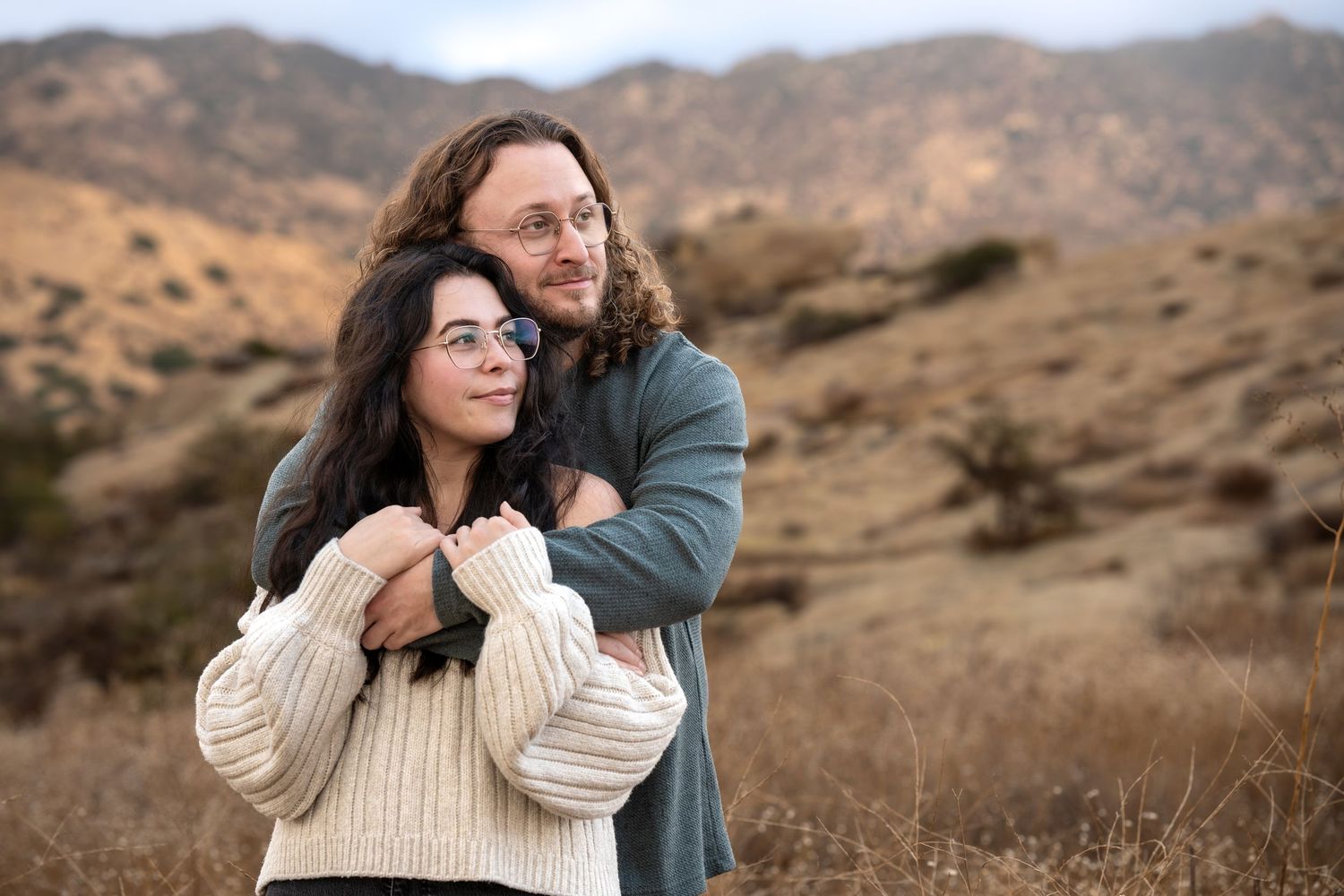 Candid couple portraits in warm sweaters against golden mountain landscape.
