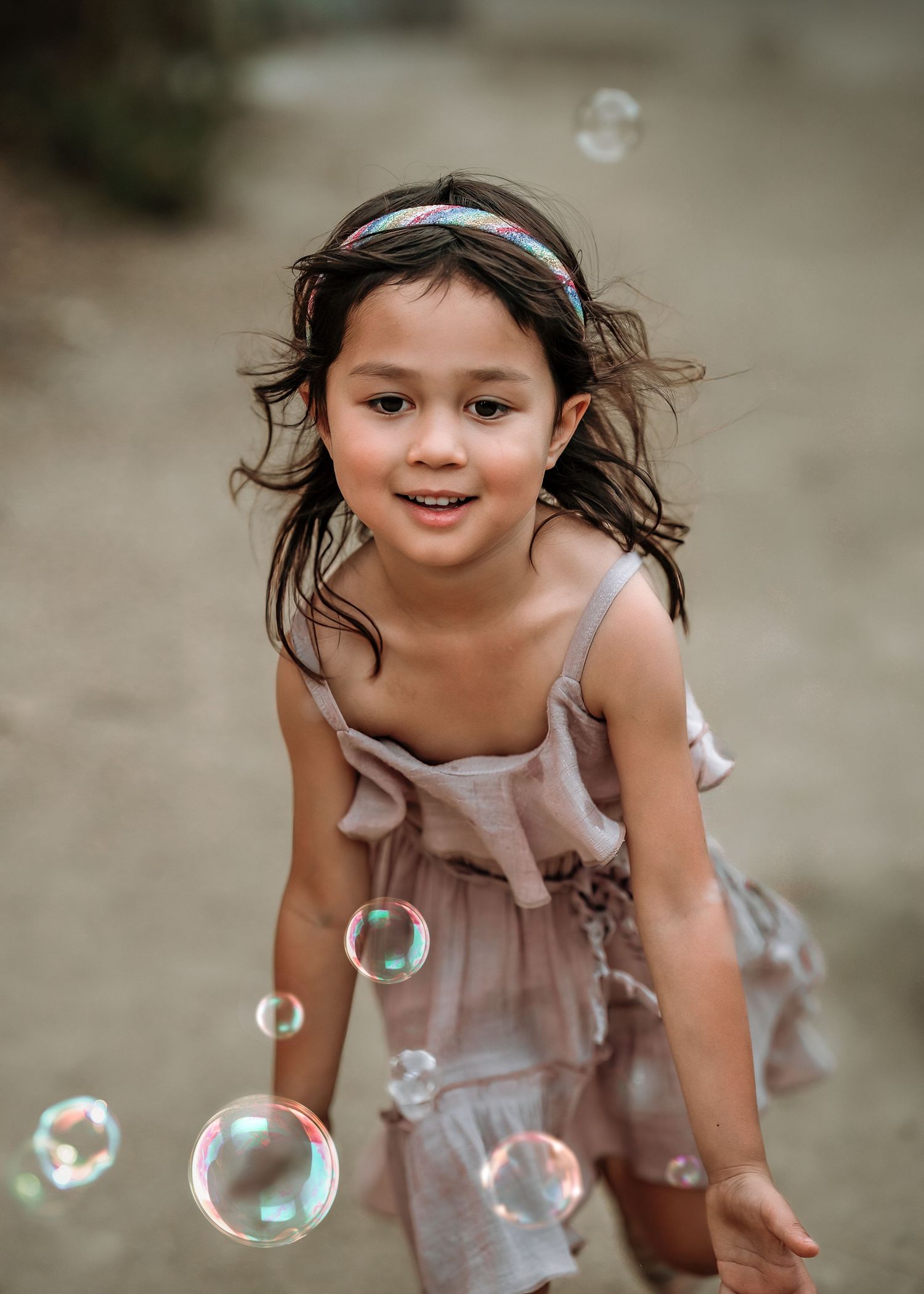 A child in a pink dress chases soap bubbles floating in the air.