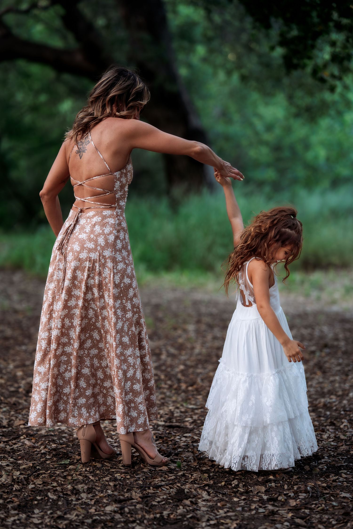 Mother and daughter dancing together on forest ground in matching floral and white dresses.