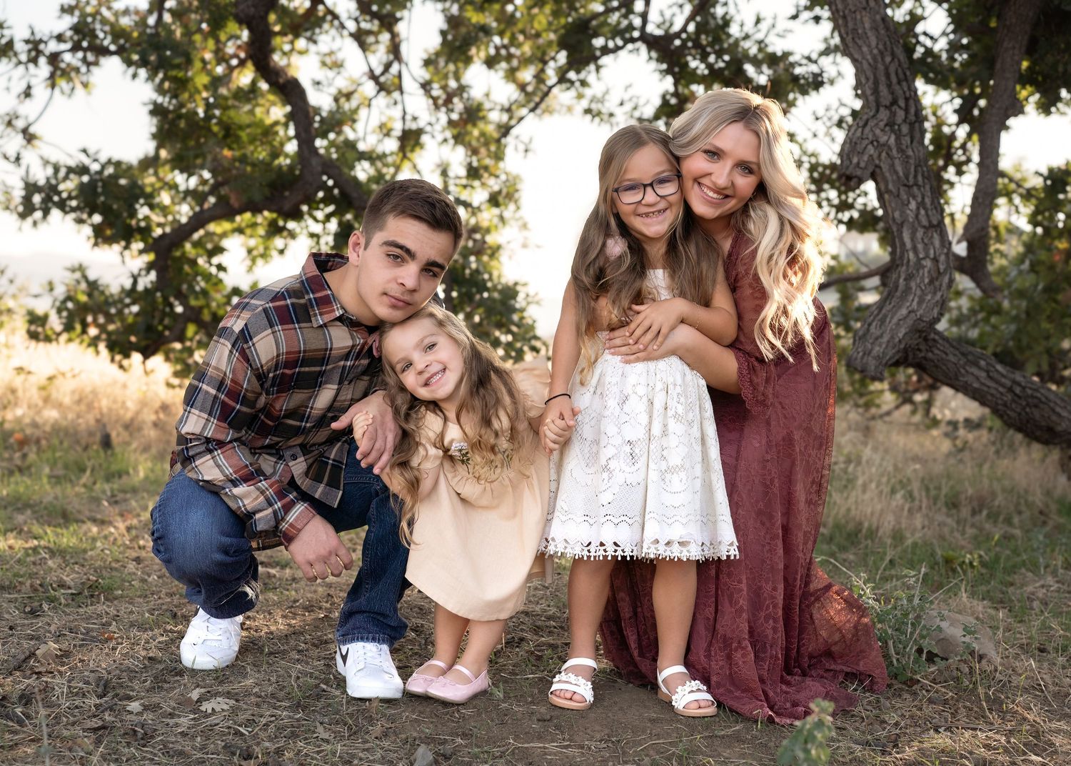 A group poses together outdoors under a tree during golden hour in coordinating casual outfits.