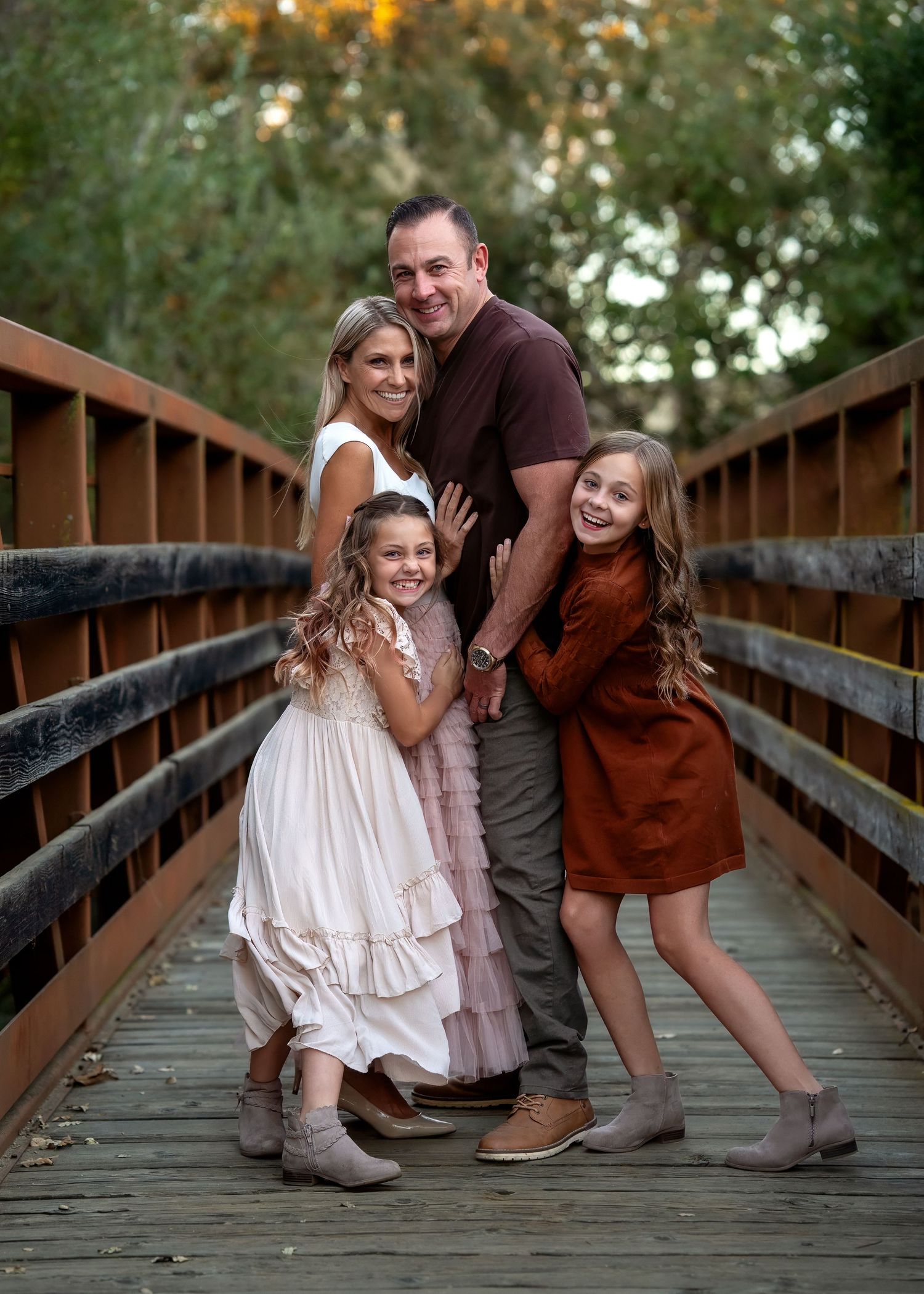 A family shares playful moments together on a wooden bridge in casual attire.