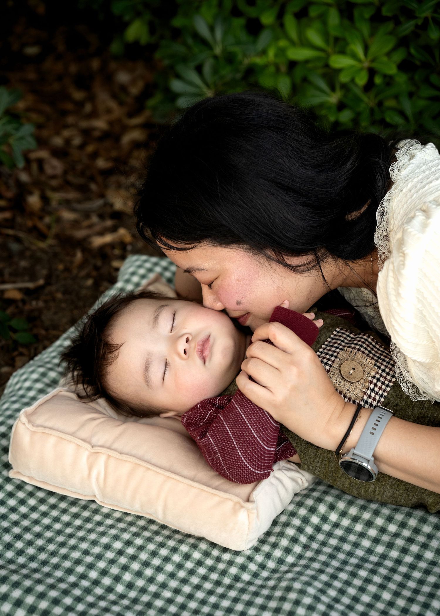 Tender moment between parent and child lying on a checkered blanket outdoors.