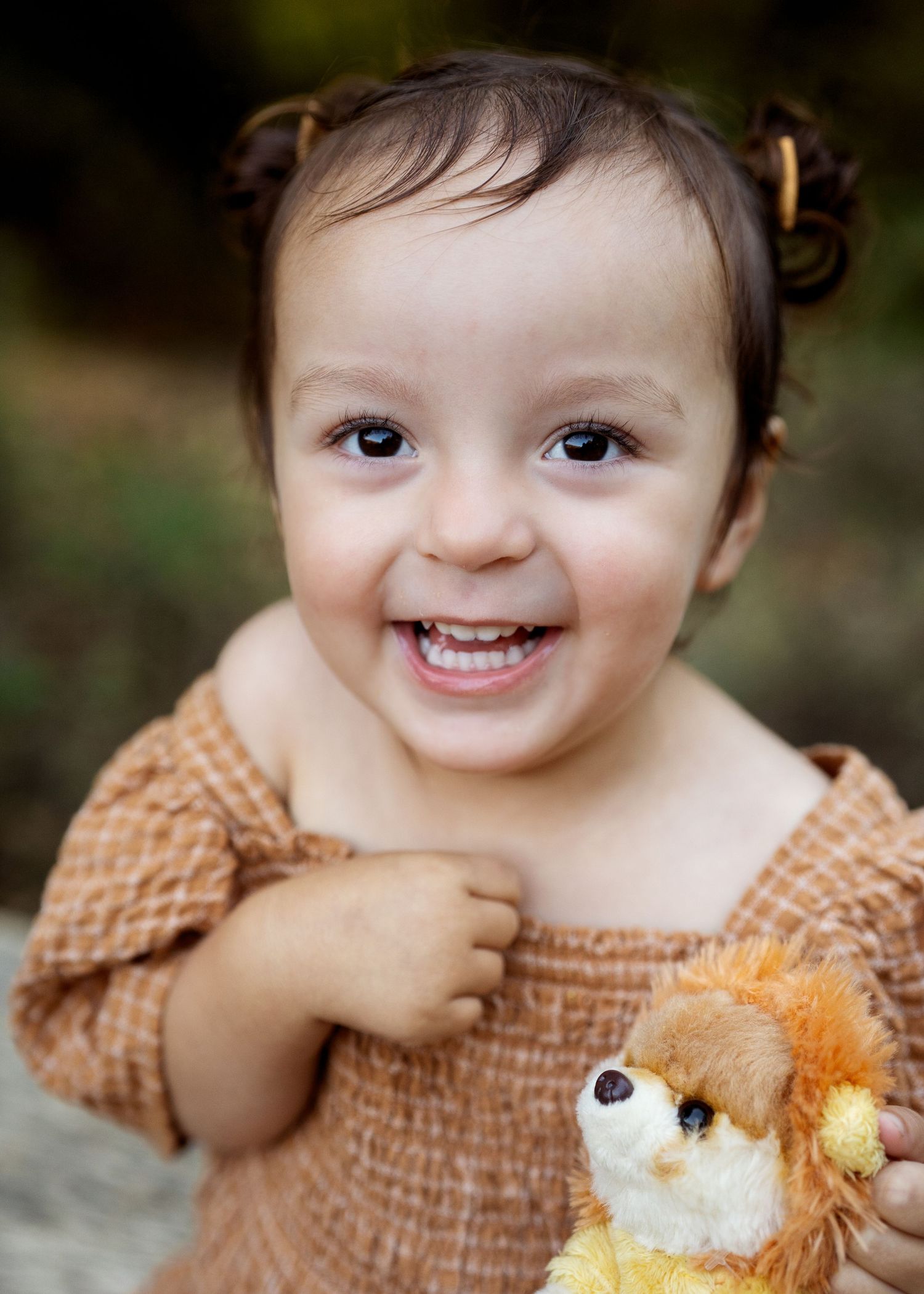 A smiling baby in a peach dress holds a plush toy.