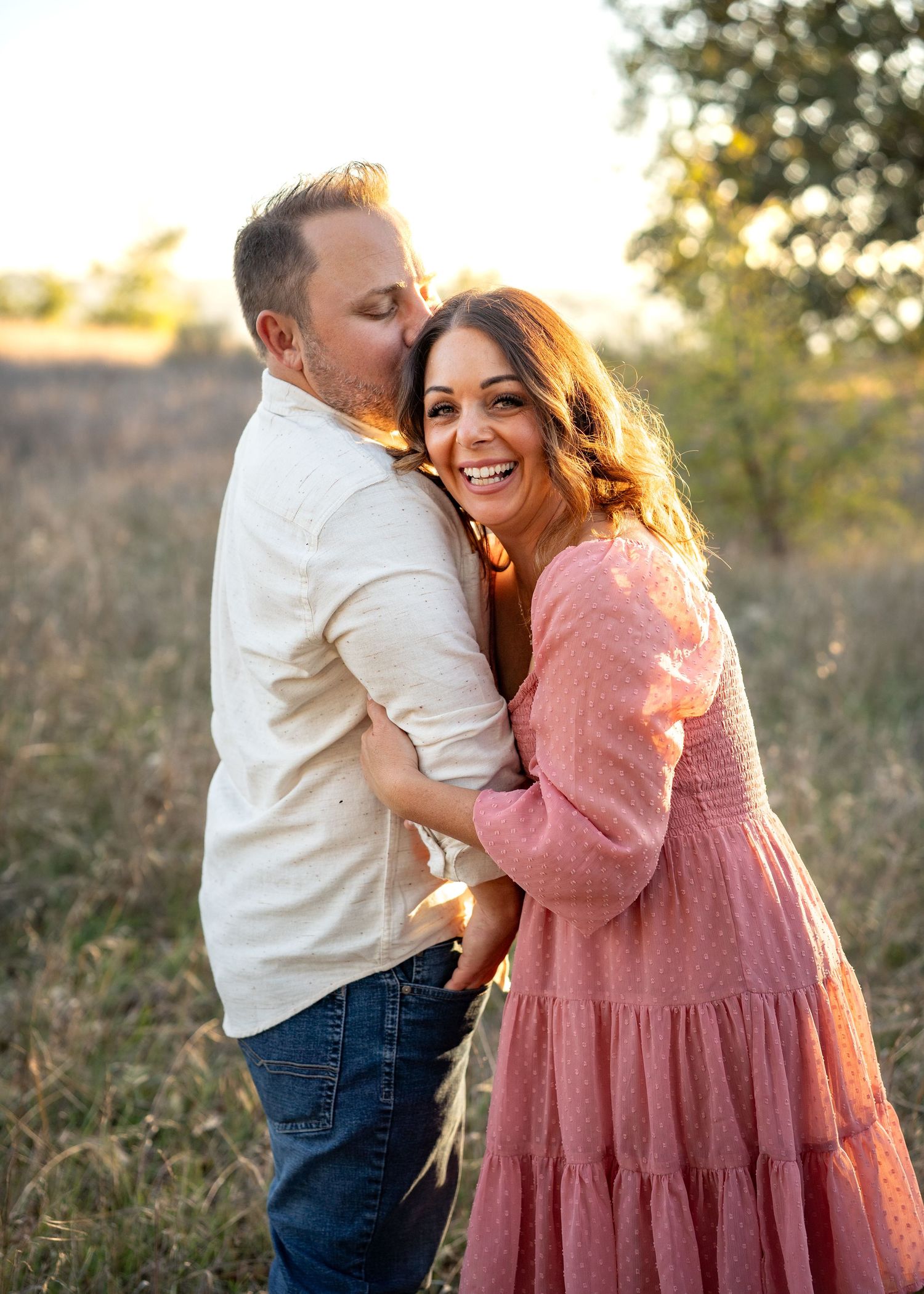 Couple laughing together in field during golden sunset light.