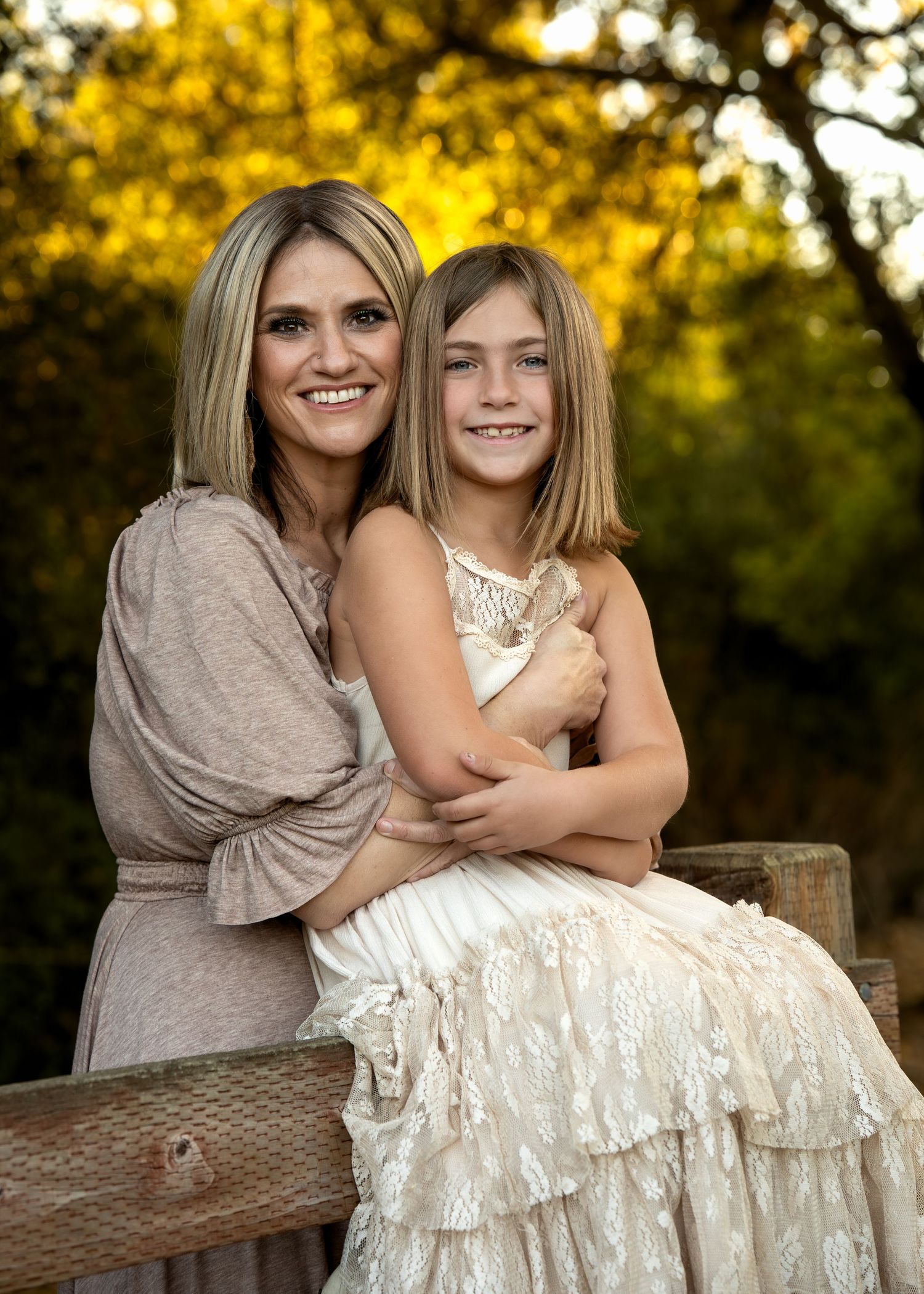 Two people pose together on a wooden fence with golden autumn foliage in the background.