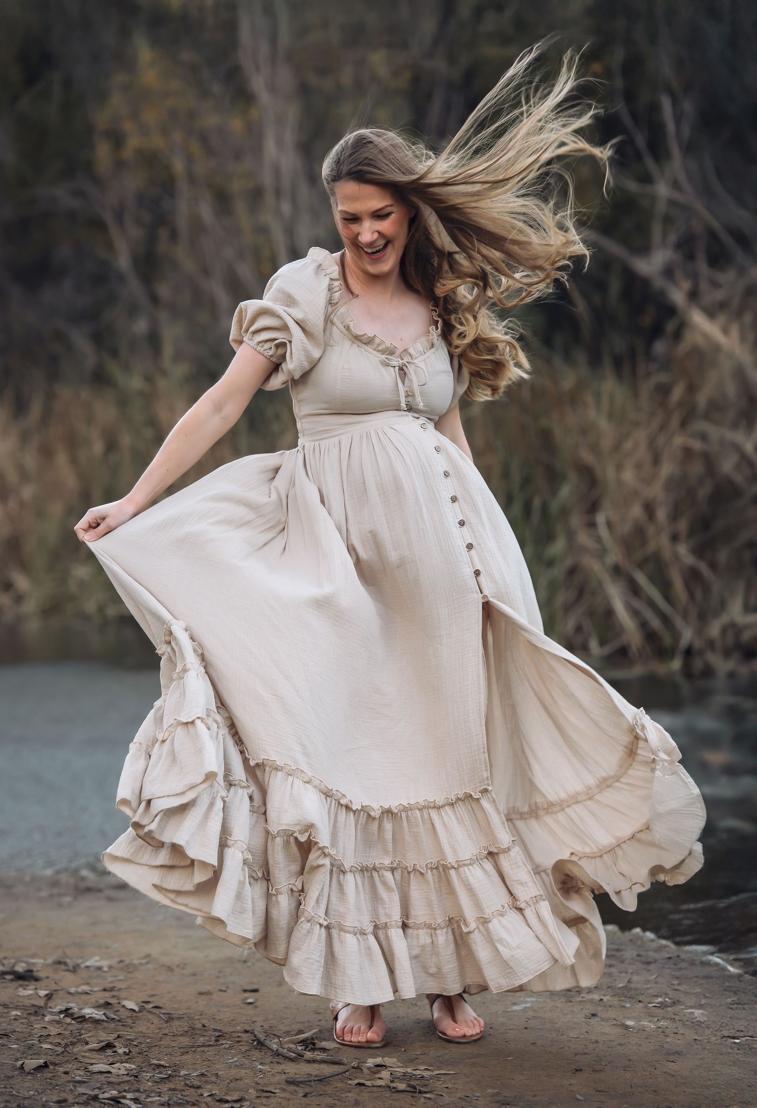 Flowing cream dress twirls gracefully during outdoor photoshoot near water.