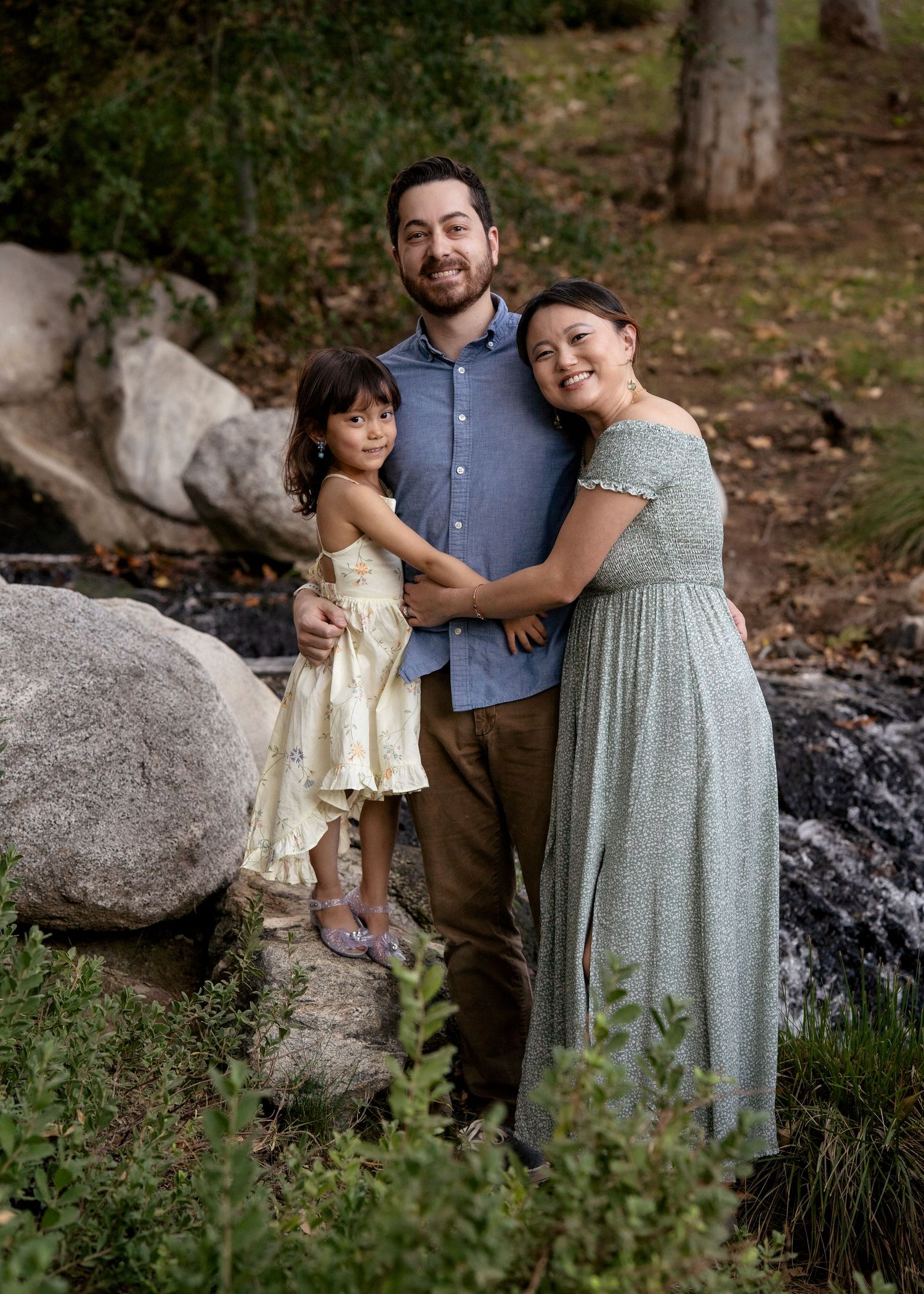 A sweet family portrait captured in nature with large boulders and trees in the background.