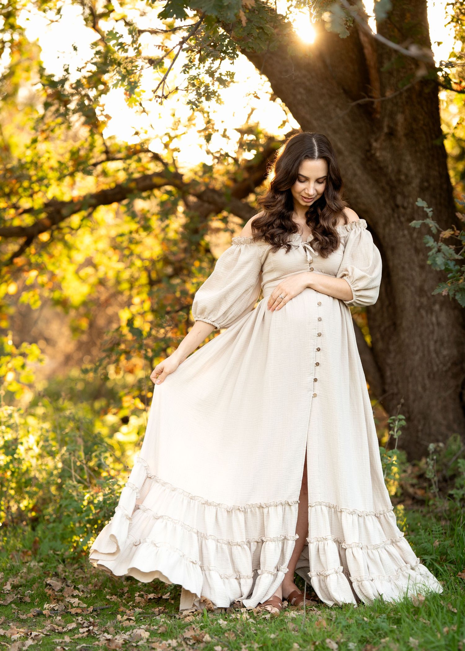 Beautiful maternity photos in a sunlit garden with flowing white dress and natural backdrop.