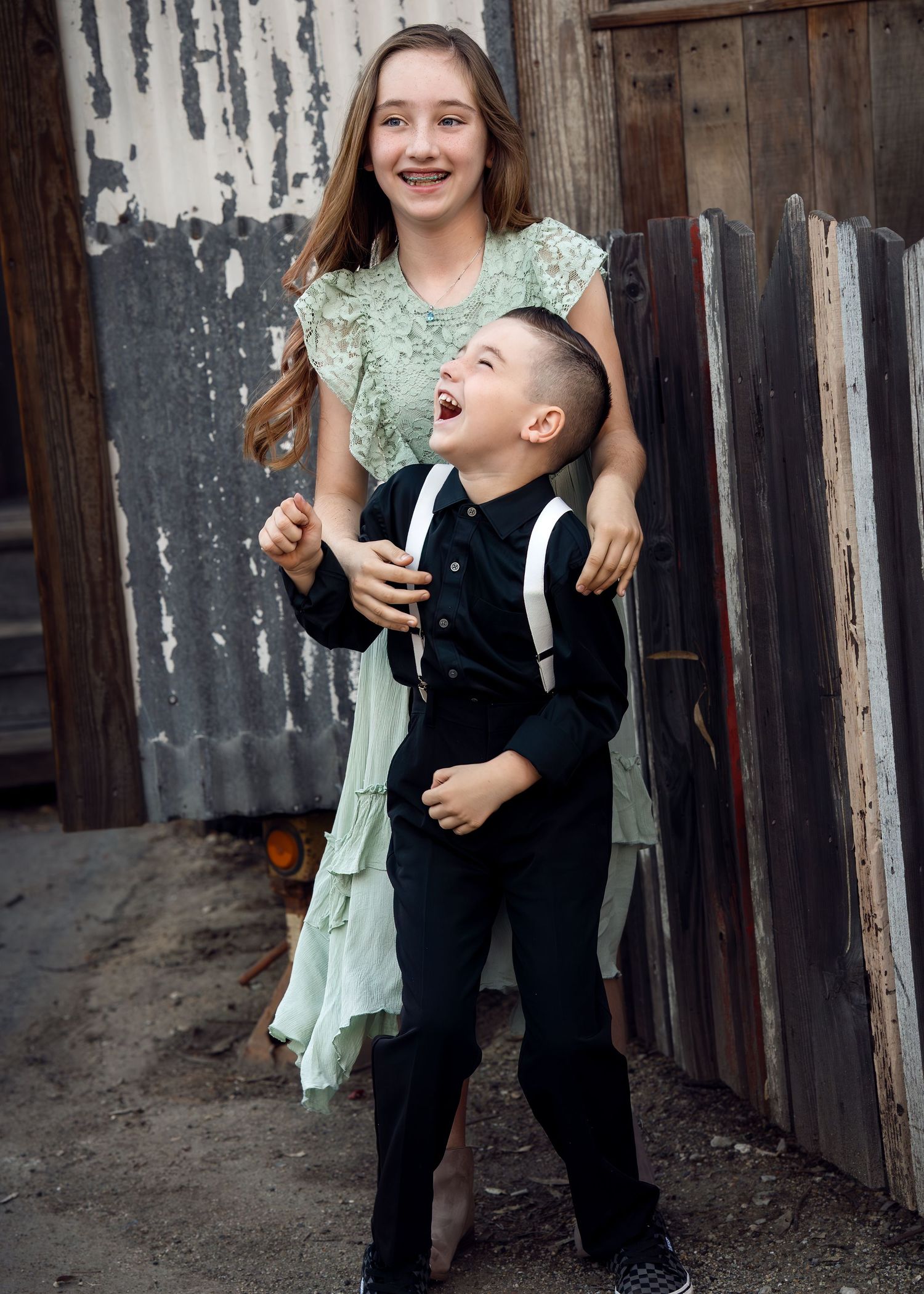 Two people share a playful moment outdoors against a rustic wooden backdrop.