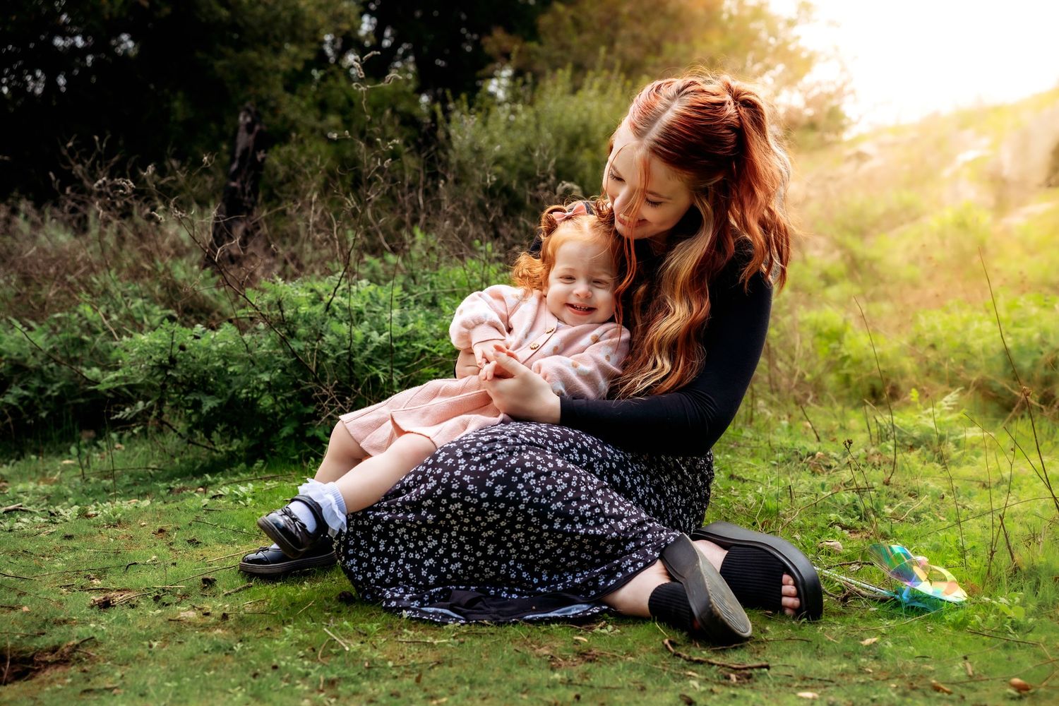 A tender outdoor moment between parent and child sitting in grass at sunset.