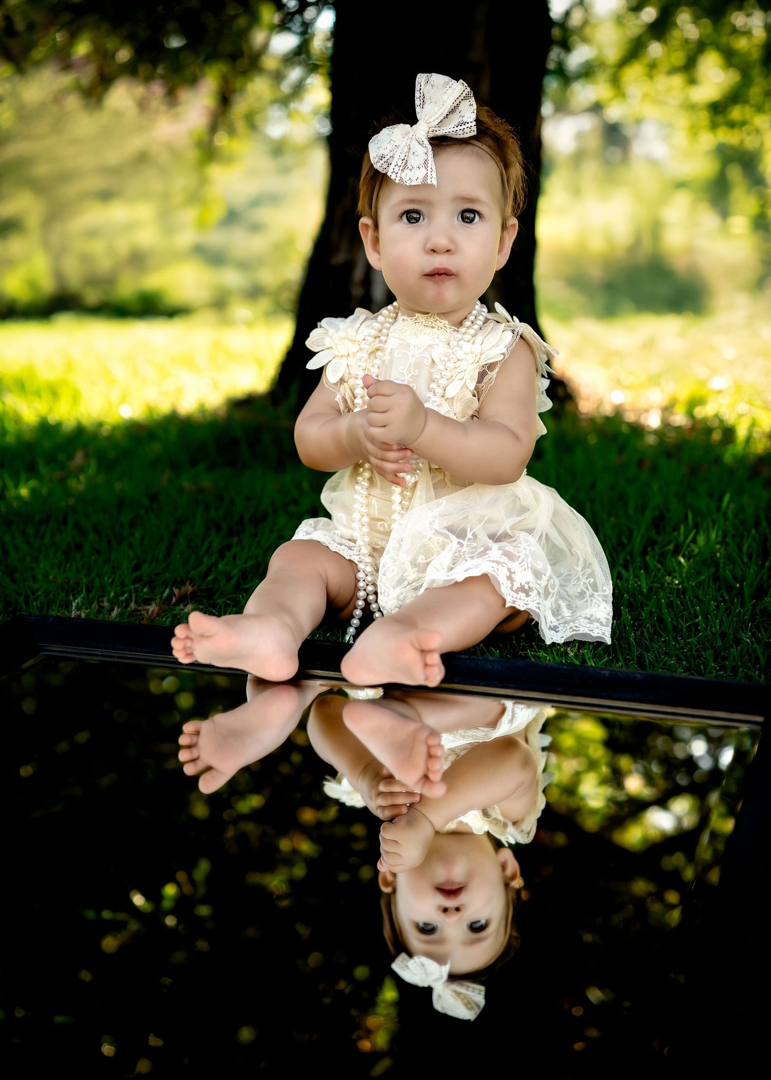 Baby wearing vintage lace dress sitting on dark surface in outdoor setting.
