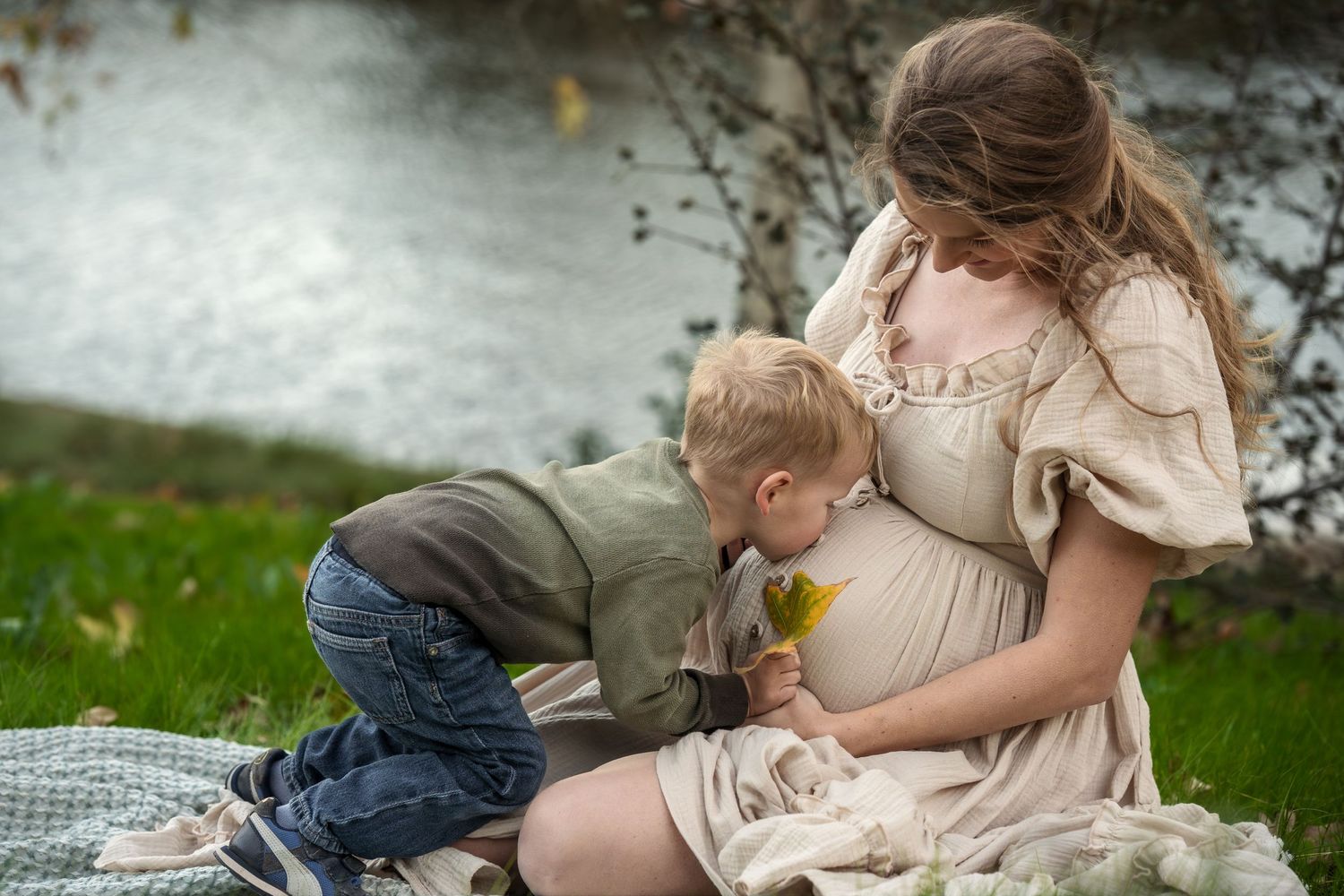 Family picnic scene with blanket spread on grass near water.