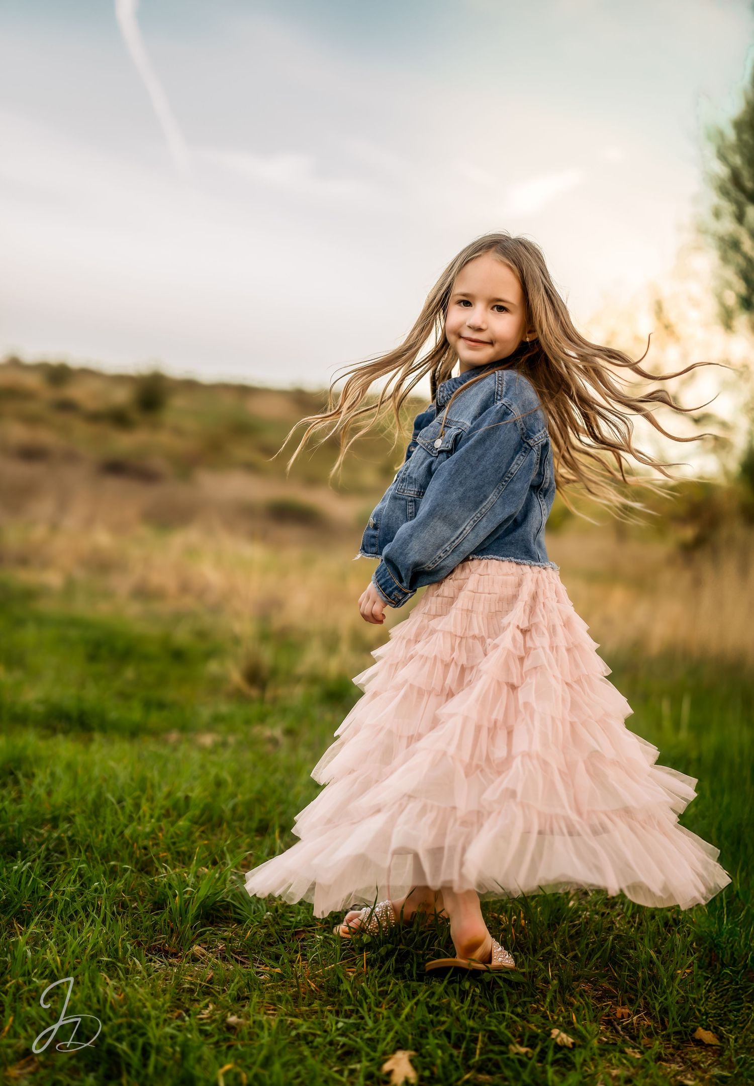 Figure in denim jacket and pink tulle skirt twirling in grassy field.