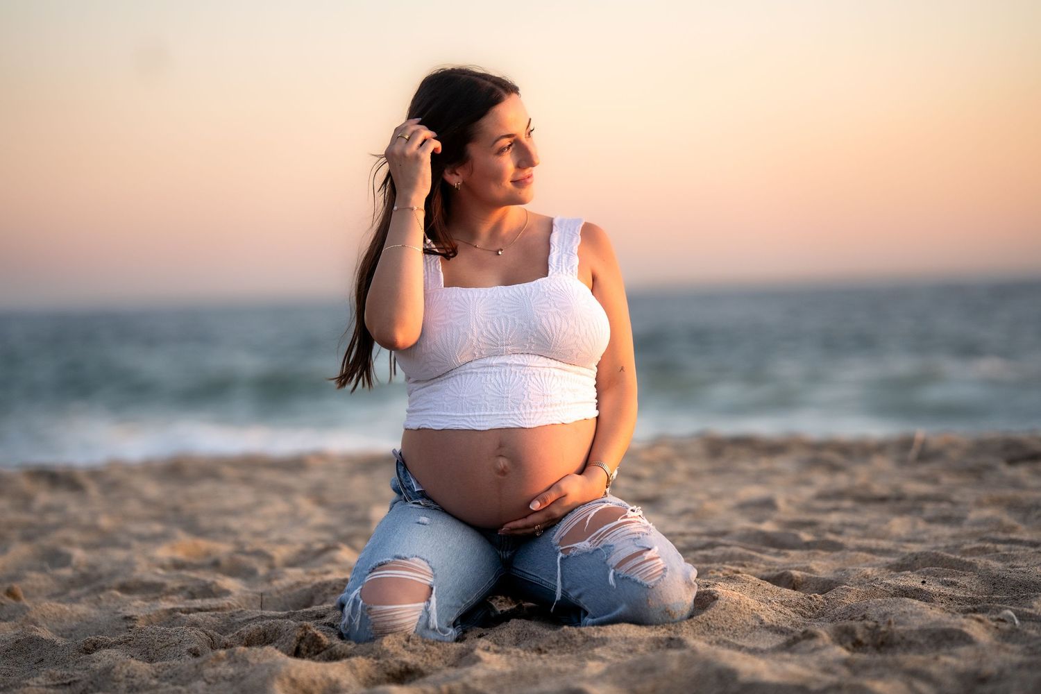 Sunset maternity session on sandy beach with ocean backdrop.
