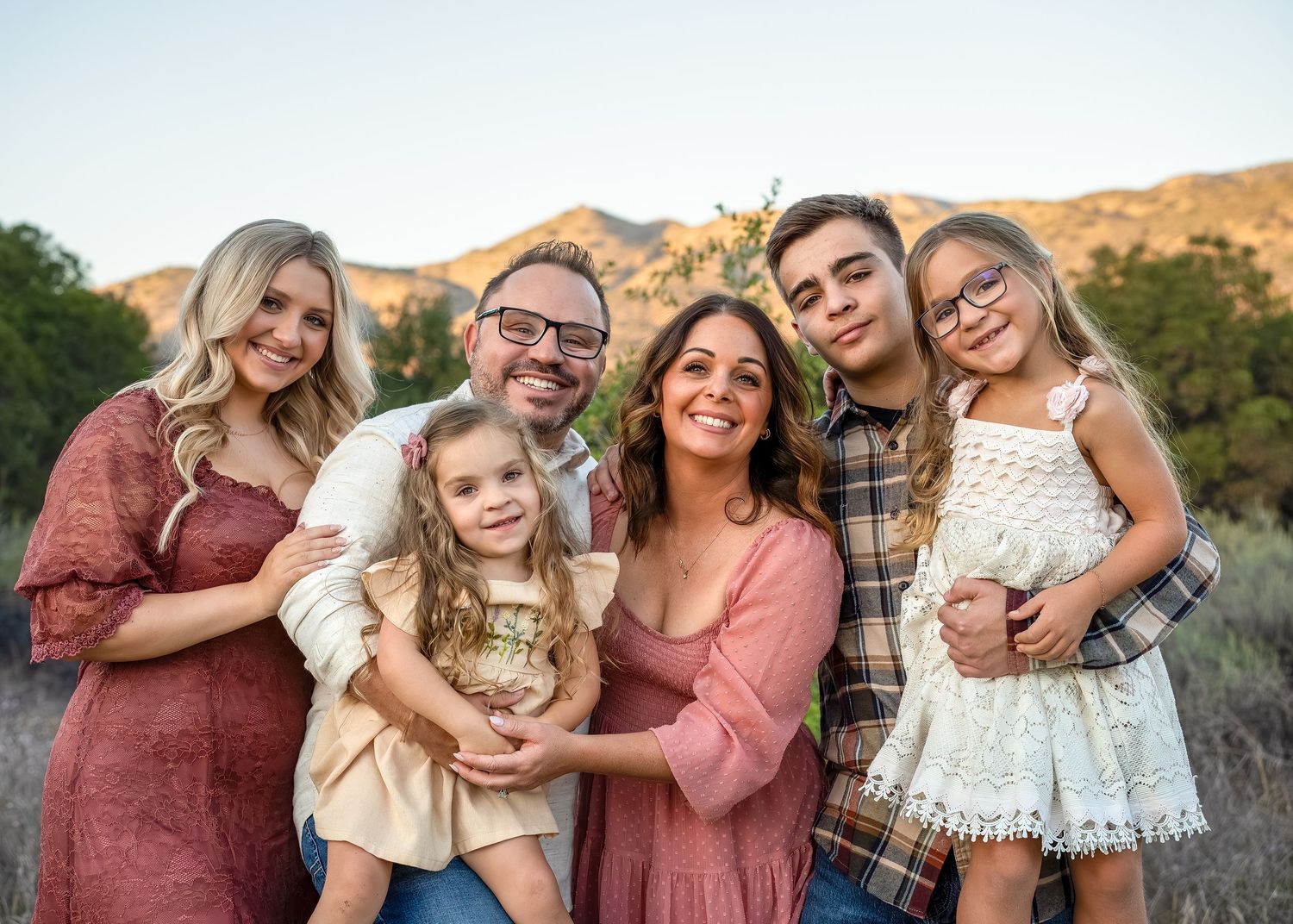 A family group poses together outdoors with mountains visible in the warm sunset light.
