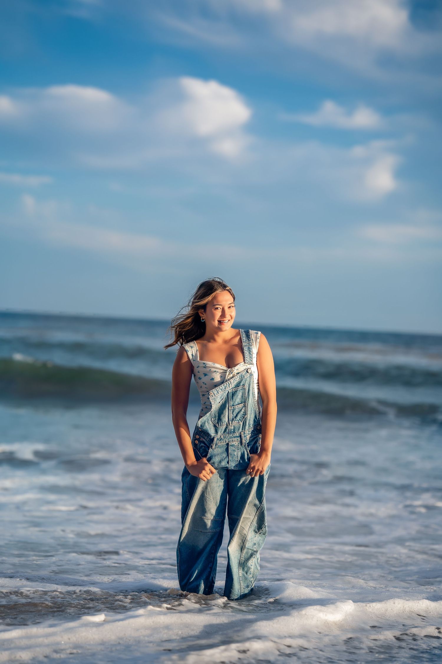 Person in blue dress plays in ocean waves during sunset photoshoot.