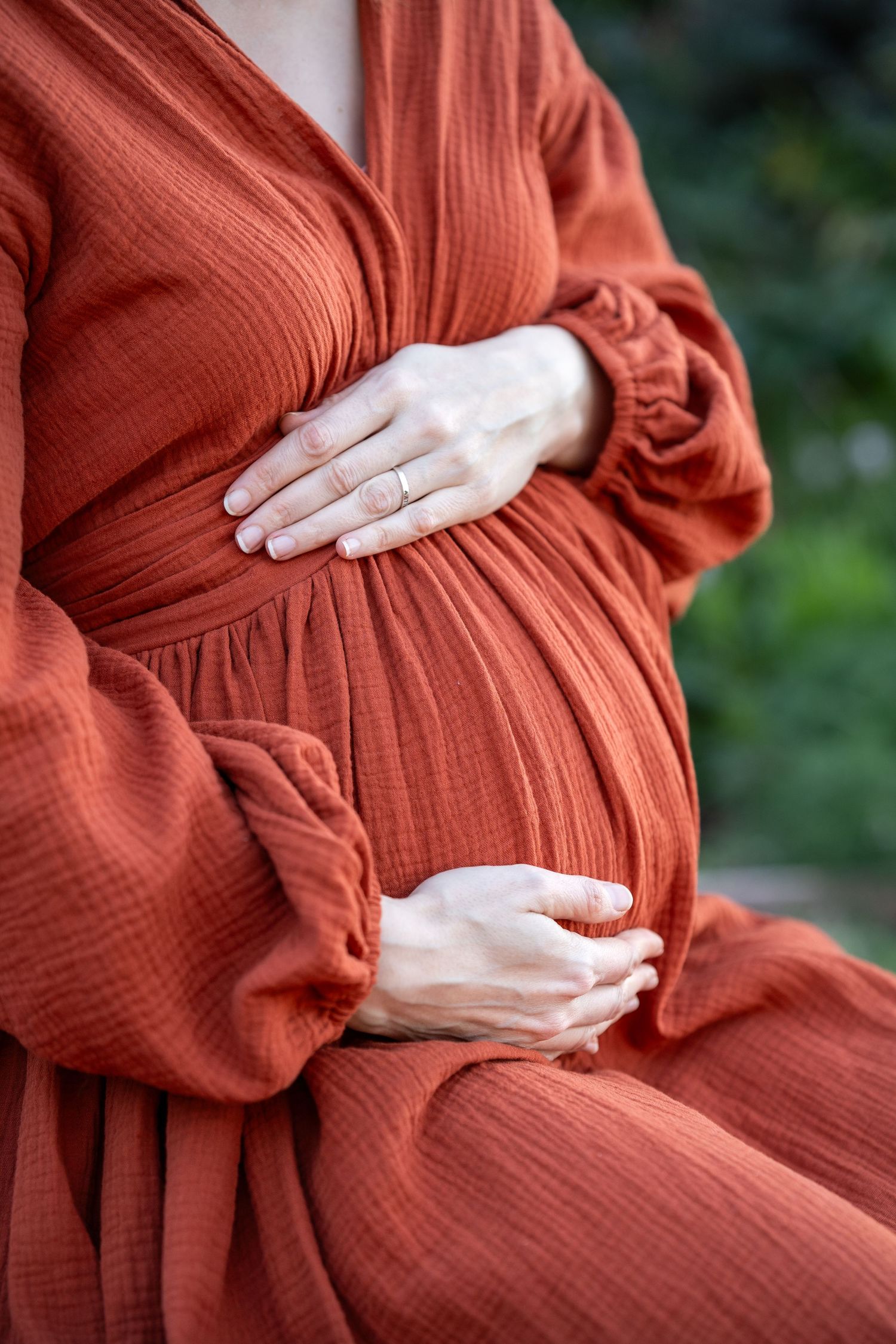A series of photos showing hands cradling a pregnant belly in a rust-colored knit dress against a natural background.
