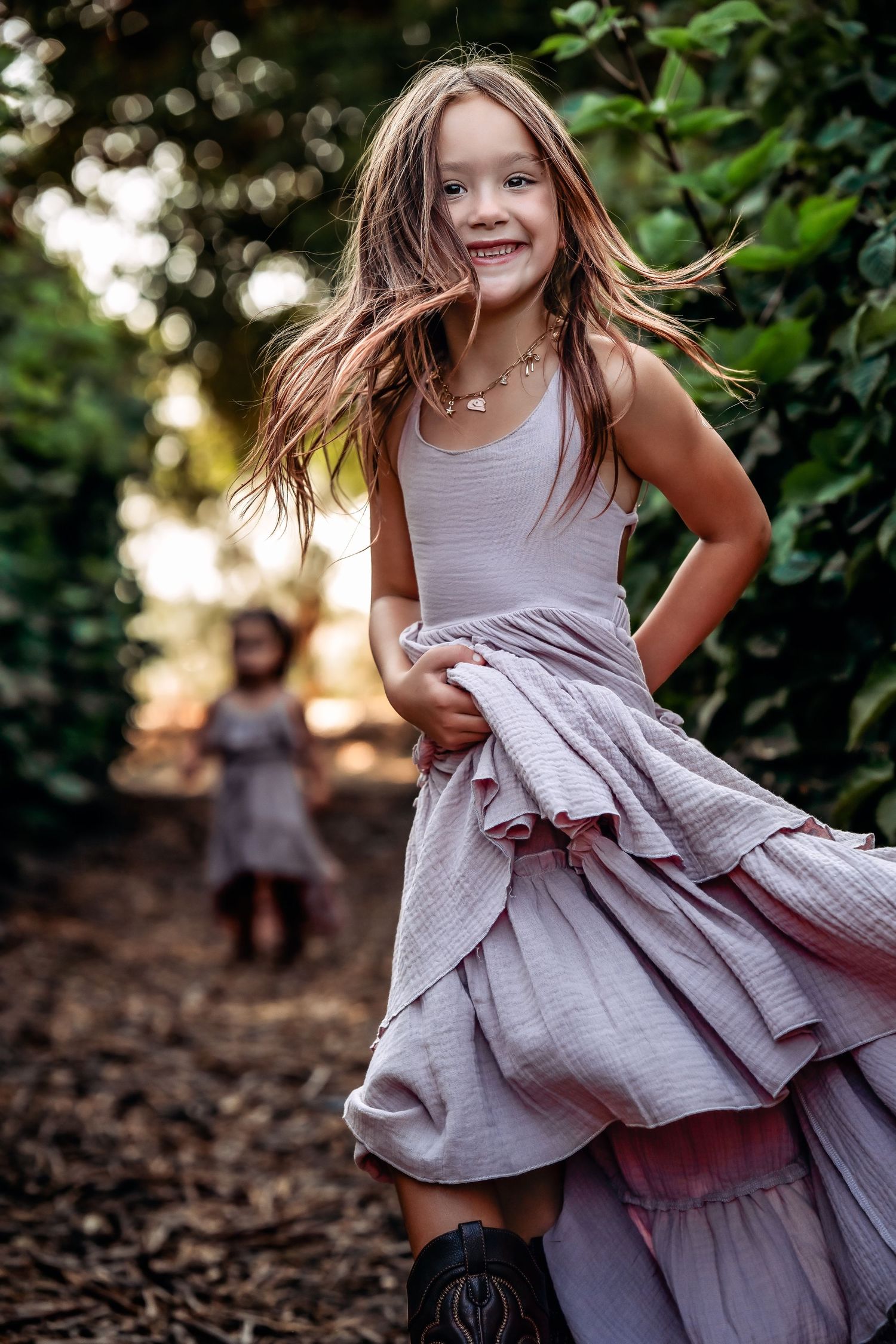 Child twirling in a flowing gray dress outdoors with natural bokeh background.