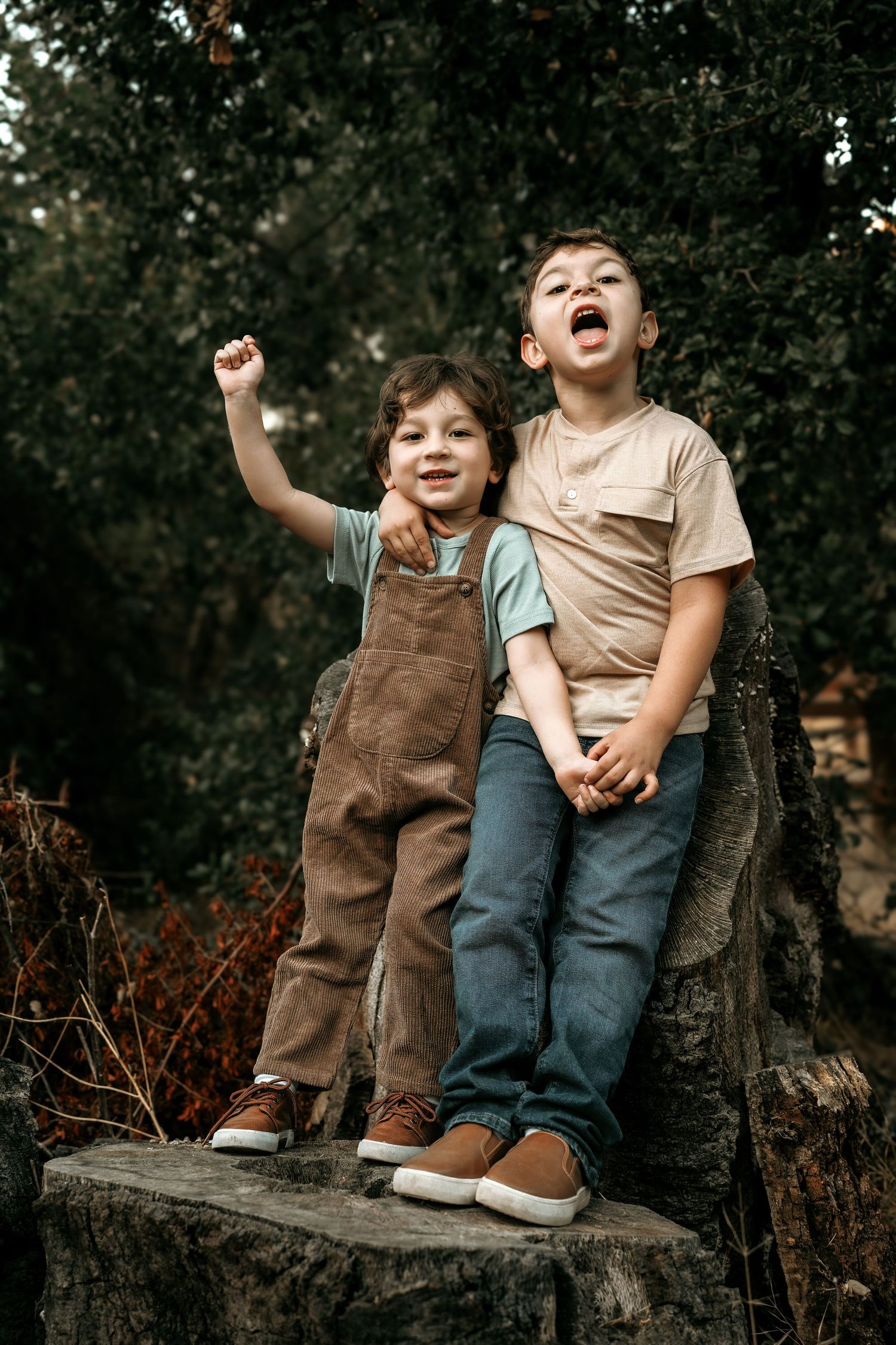 Two children sit together on a wooden log in casual clothing.