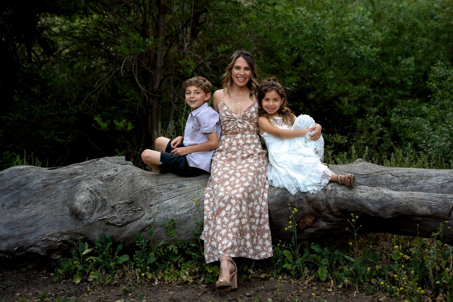 Family sitting together on a fallen log in a lush green forest setting.