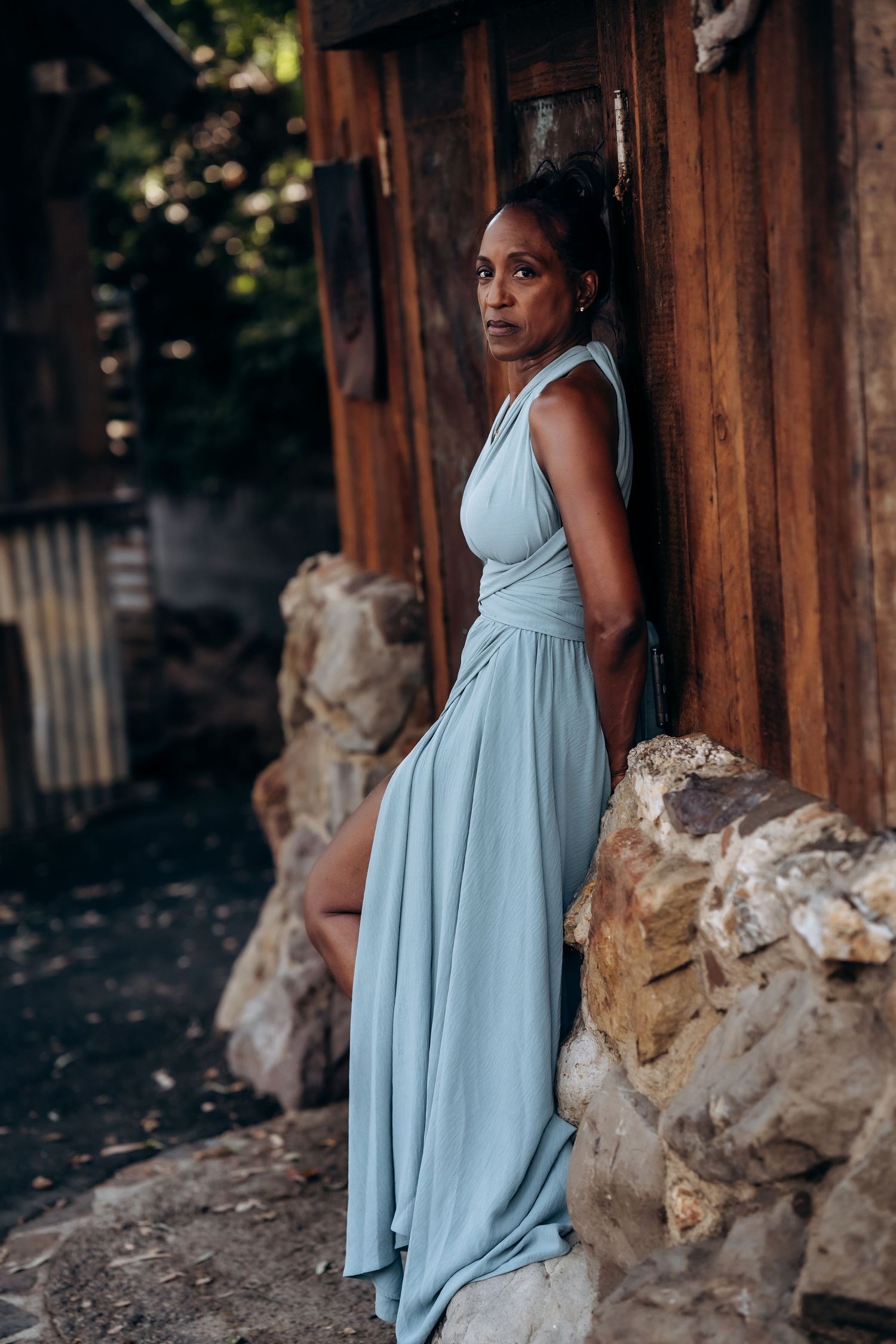 A flowing light blue dress is photographed in an artistic sequence against weathered wood and stone.