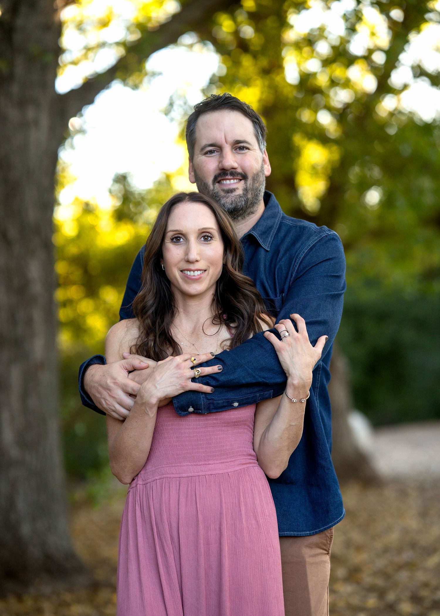 Couple embracing outdoors with woman in pink dress and man in navy blazer.
