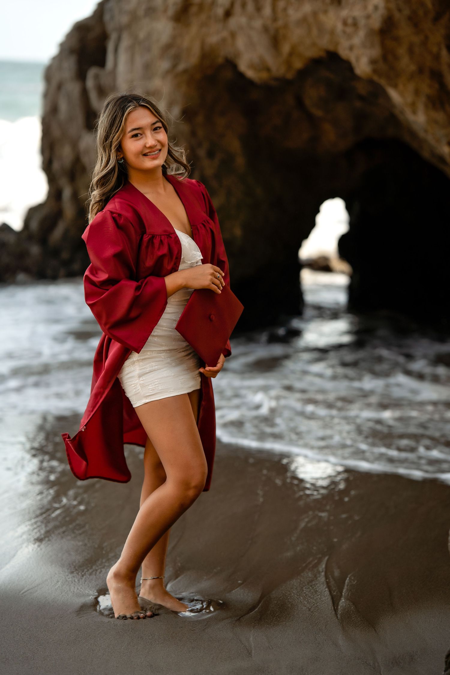 Beachside portraits at rocky cave formations with red jacket styling.