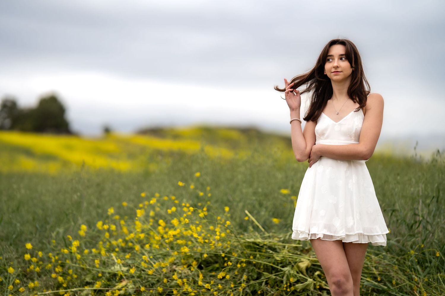 Graduation photoshoot in white dress among blooming yellow wildflowers.