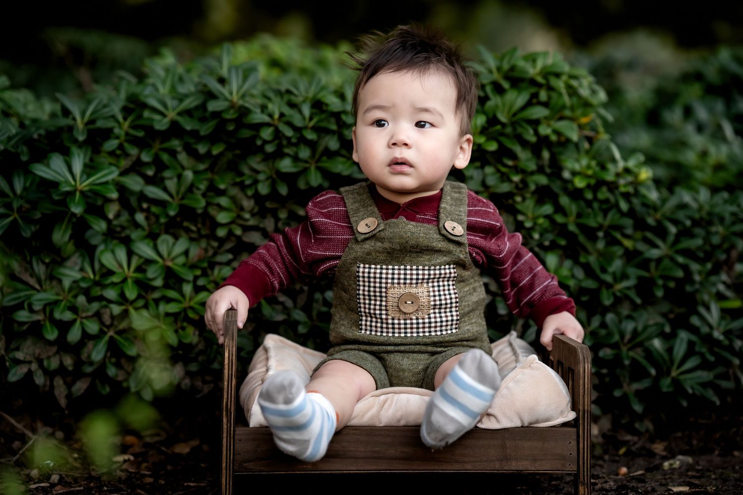 Baby sitting in a vintage wooden chair against a green garden backdrop.