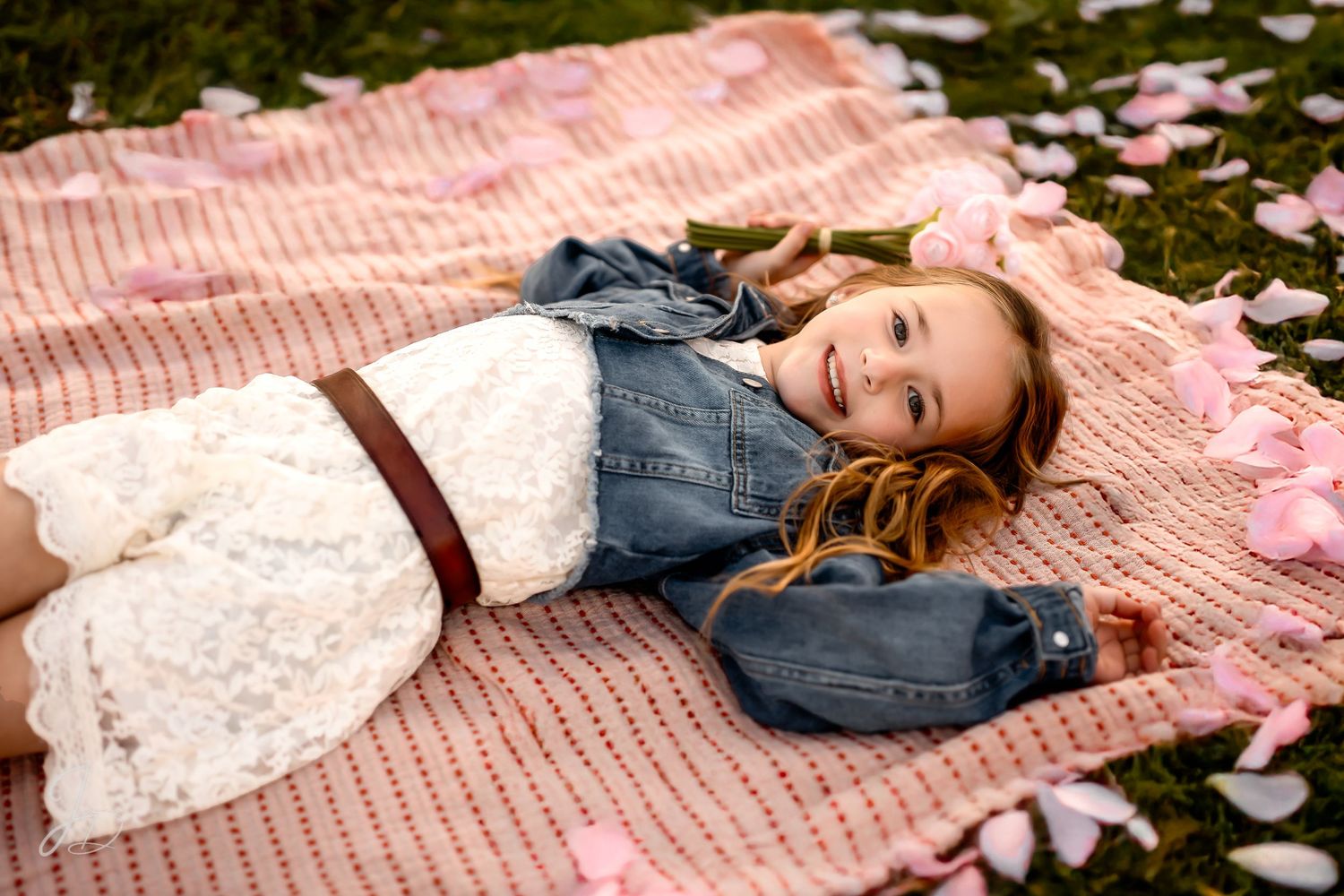 Person in denim jacket lying on pink blanket surrounded by flower petals.