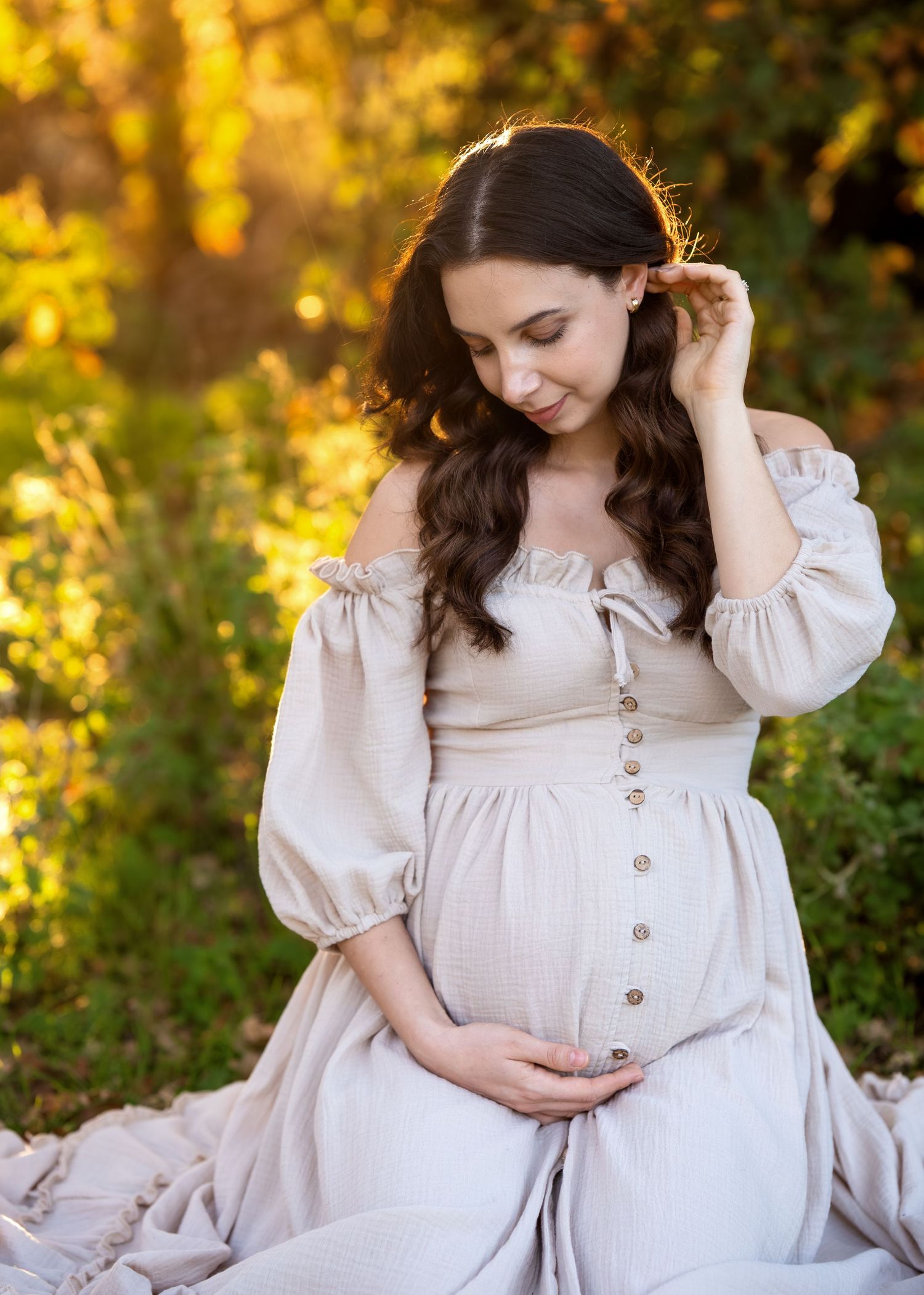 Maternity photoshoot in a garden setting with warm golden sunlight filtering through trees.