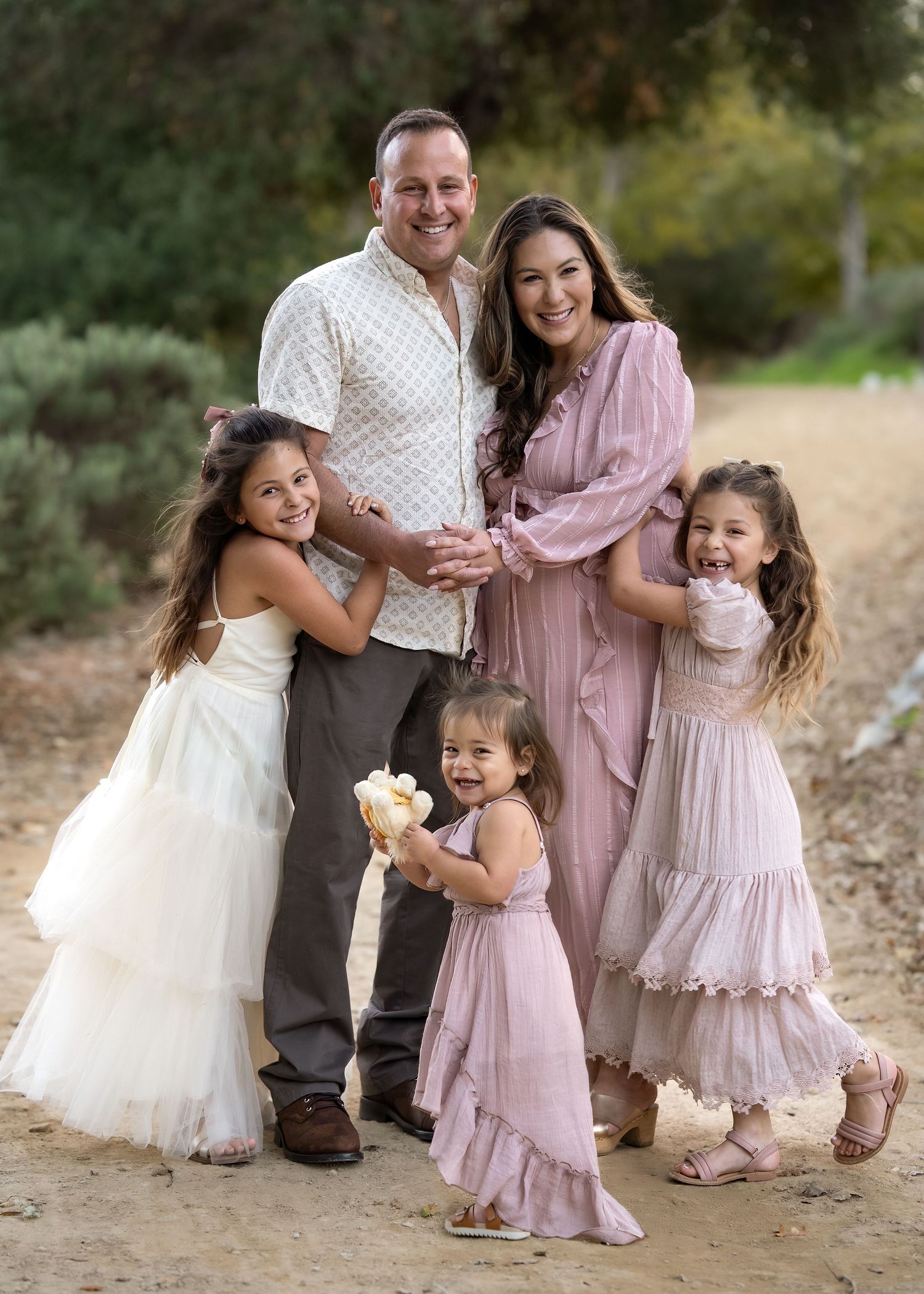 Family wearing coordinated pink and white outfits poses together on a dirt path during golden hour.
