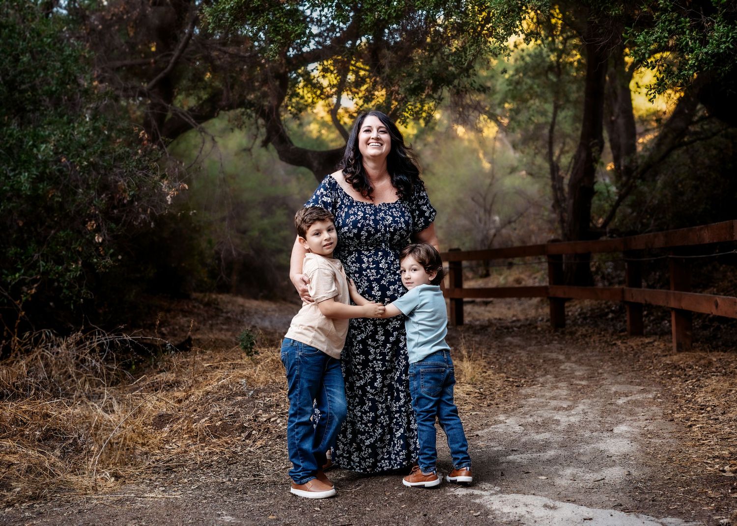 A casual family photoshoot takes place on a rustic outdoor path surrounded by trees.