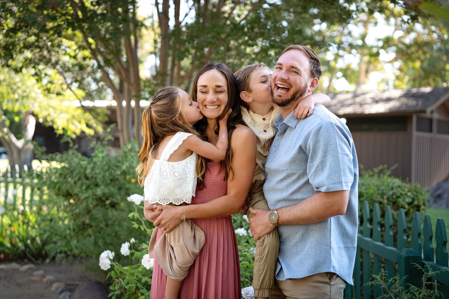 A joyful family shares an intimate moment of laughter and hugs in a sunny garden setting.