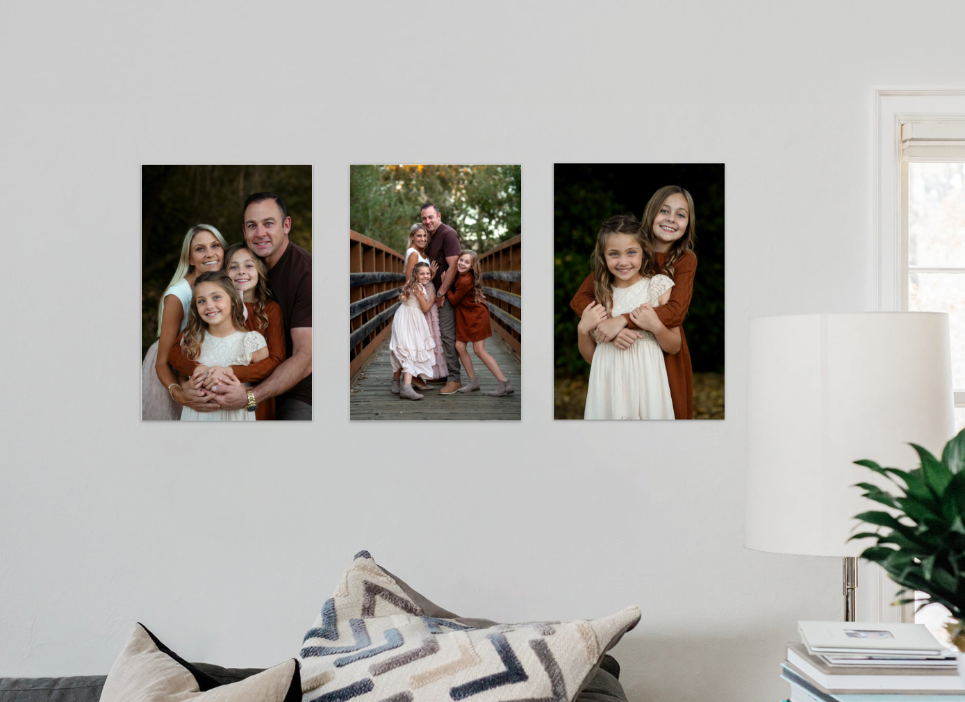 Three framed family portraits displayed on a white wall above a couch with chevron pillows and a potted plant nearby.