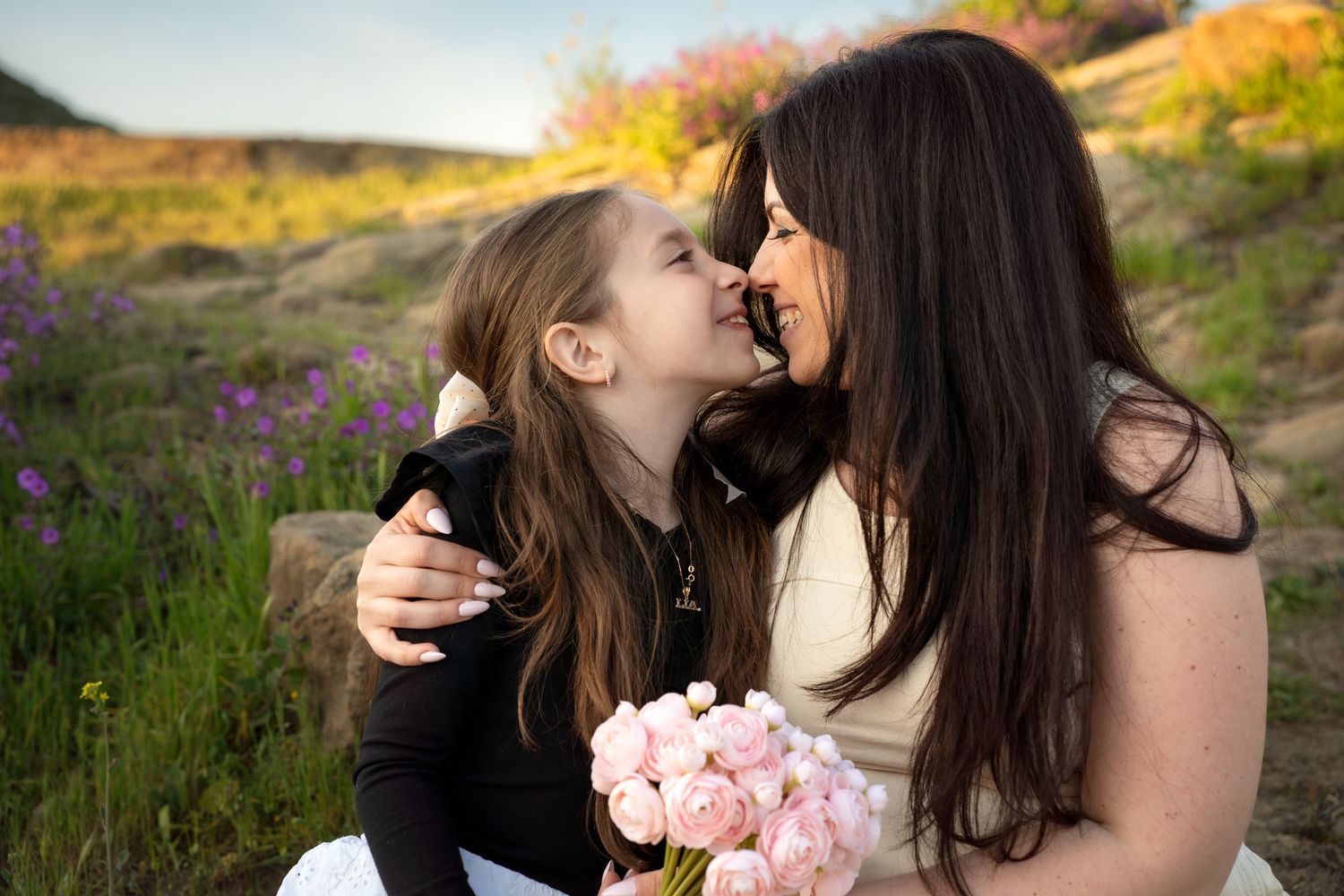 Tender moment between parent and child among wildflowers holding pink bouquet.