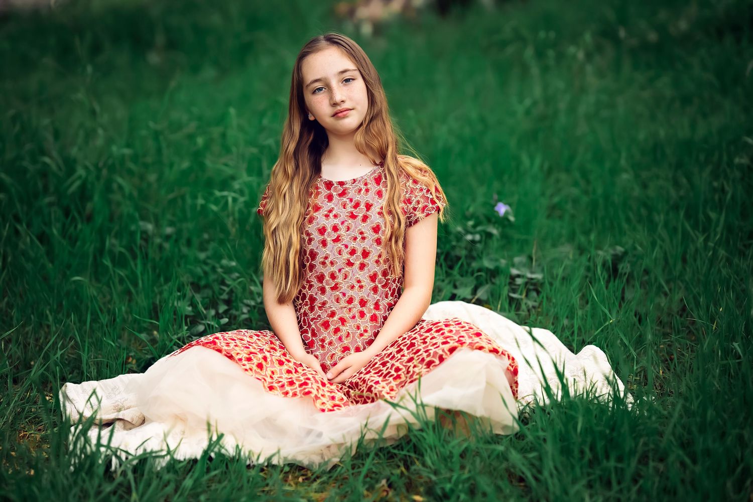 Young figure in a pink polka dot dress sitting in lush green grass on a sunny day.